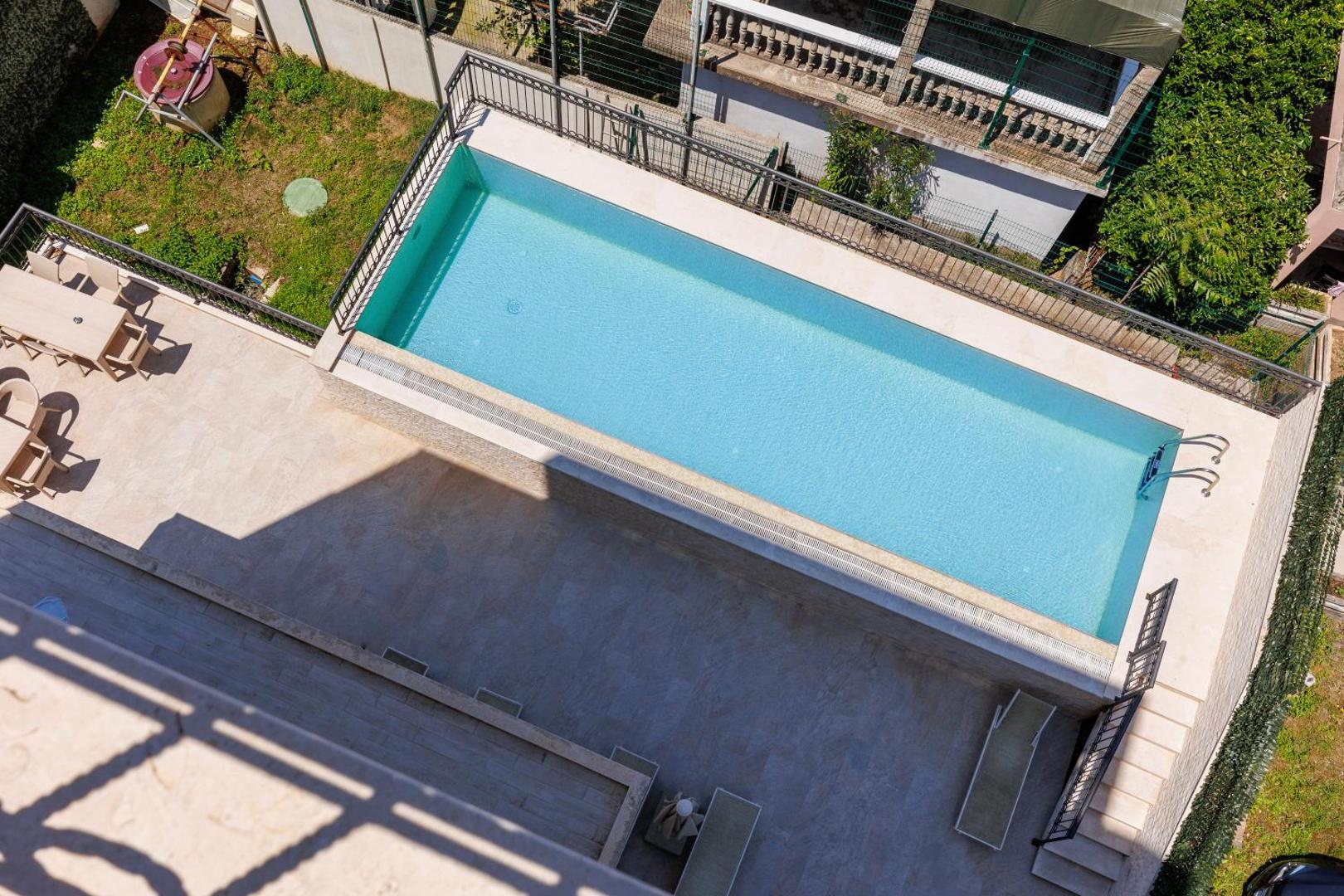 Hotel Kadmo āra baseins ar gaišu flīžu klājumu un atpūtas zonu, skats no augšas uz viesnīcas teritoriju Budvā