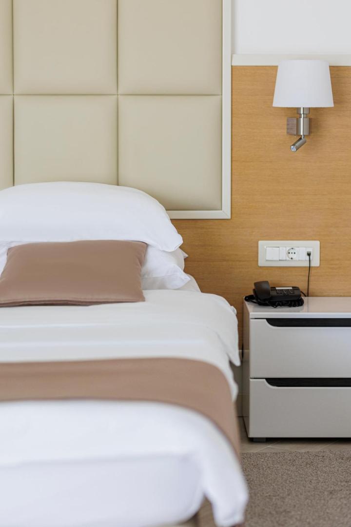 Tuvplāns Hotel Kadmo by Aycon numura gultai ar baltu veļu, naktsskapīti un modernu apgaismojumu — tīrs un minimālistisks dizains