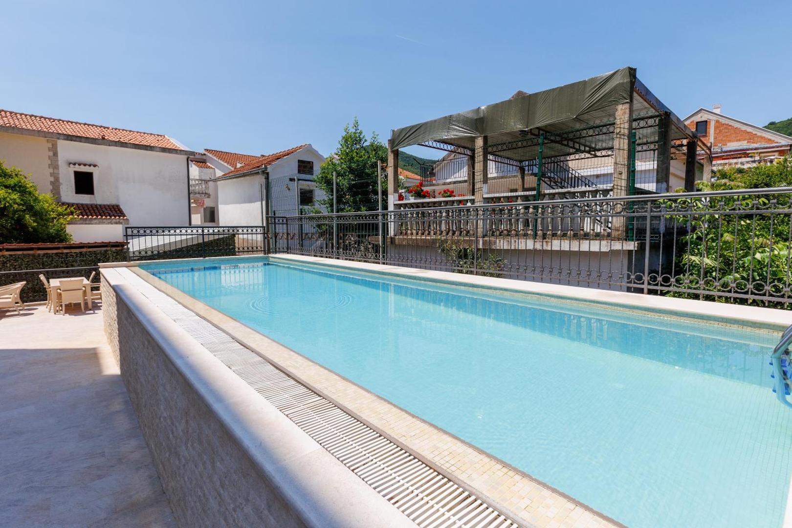 Hotel Kadmo by Aycon āra baseins uz terases Budvā — zils ūdens, sauļošanās zona un skats uz apkārtnes arhitektūru