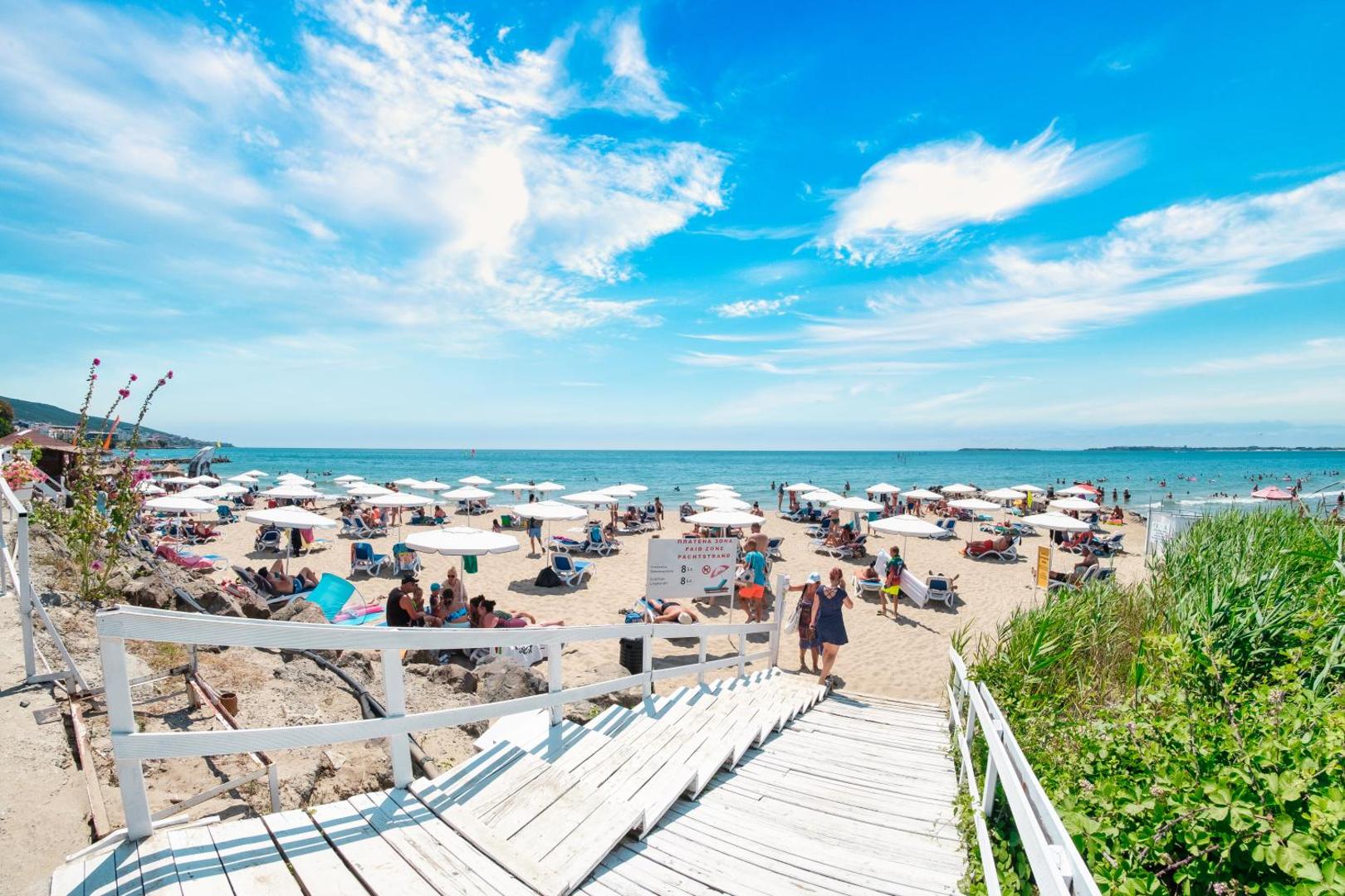 Koka kāpnes ved uz Premier Fort Beach Hotel pludmali ar daudziem baltiem saulessargiem un zilu debesu fonu