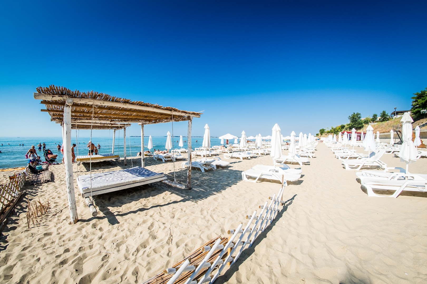 Premier Fort Beach Hotel privātā pludmale ar baltiem saulessargiem, sauļošanās krēsliem un koka nojumi Saulainajā krastā, Bulgārijā