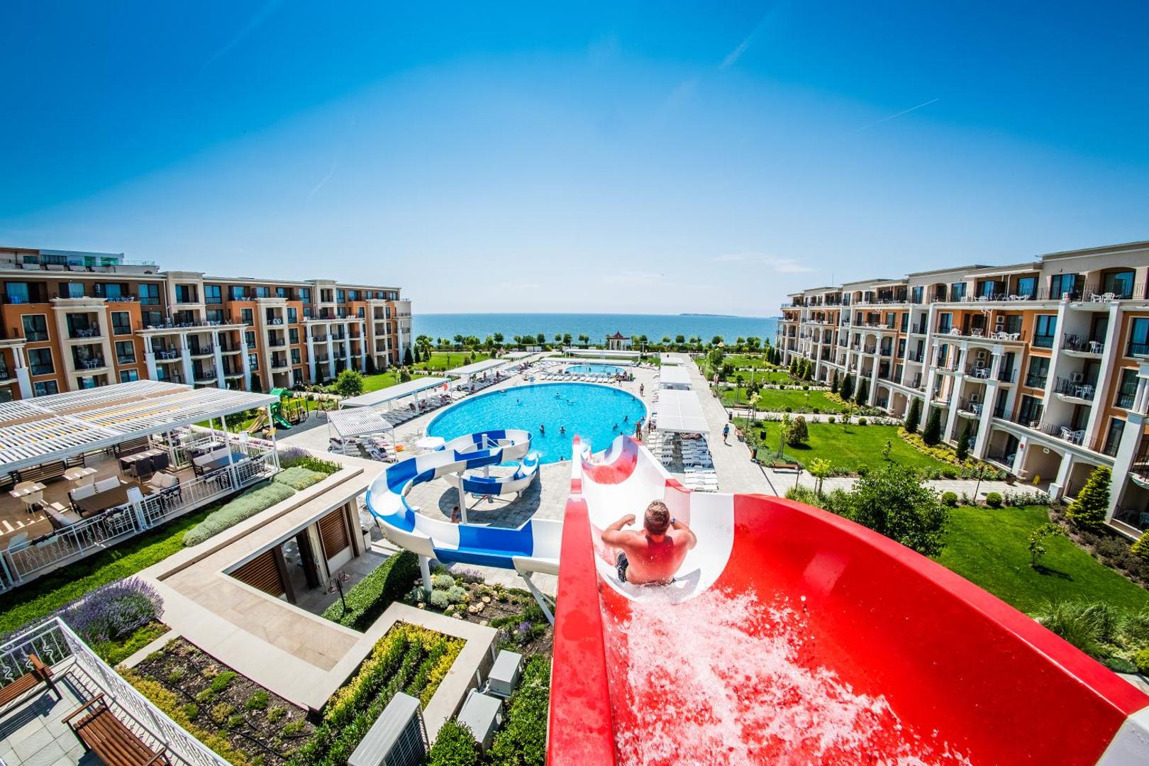 Skats no ūdens slidkalniņa virsotnes uz Premier Fort Beach Hotel baseinu, dārzu un jūras horizontu saulainā laikā