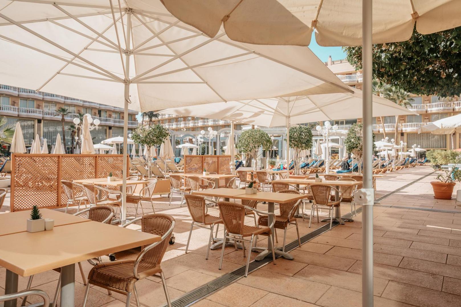 Cleopatra Palace viesnīcas atpūtas zona ar galdiņiem un lieliem saulessargiem pie baseina Tenerifē