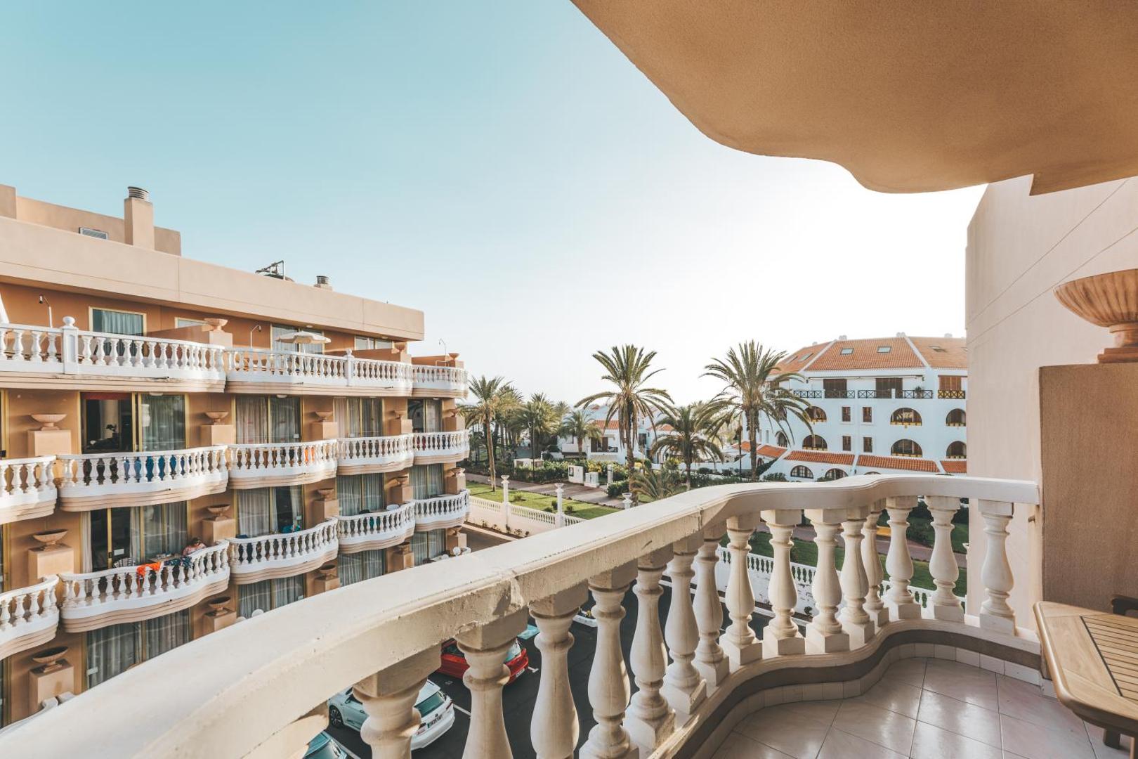Cleopatra Palace viesnīcas numura balkons ar klasiskām margām un skatu uz apkārtējo arhitektūru un palmām Tenerifē, Spānijā.