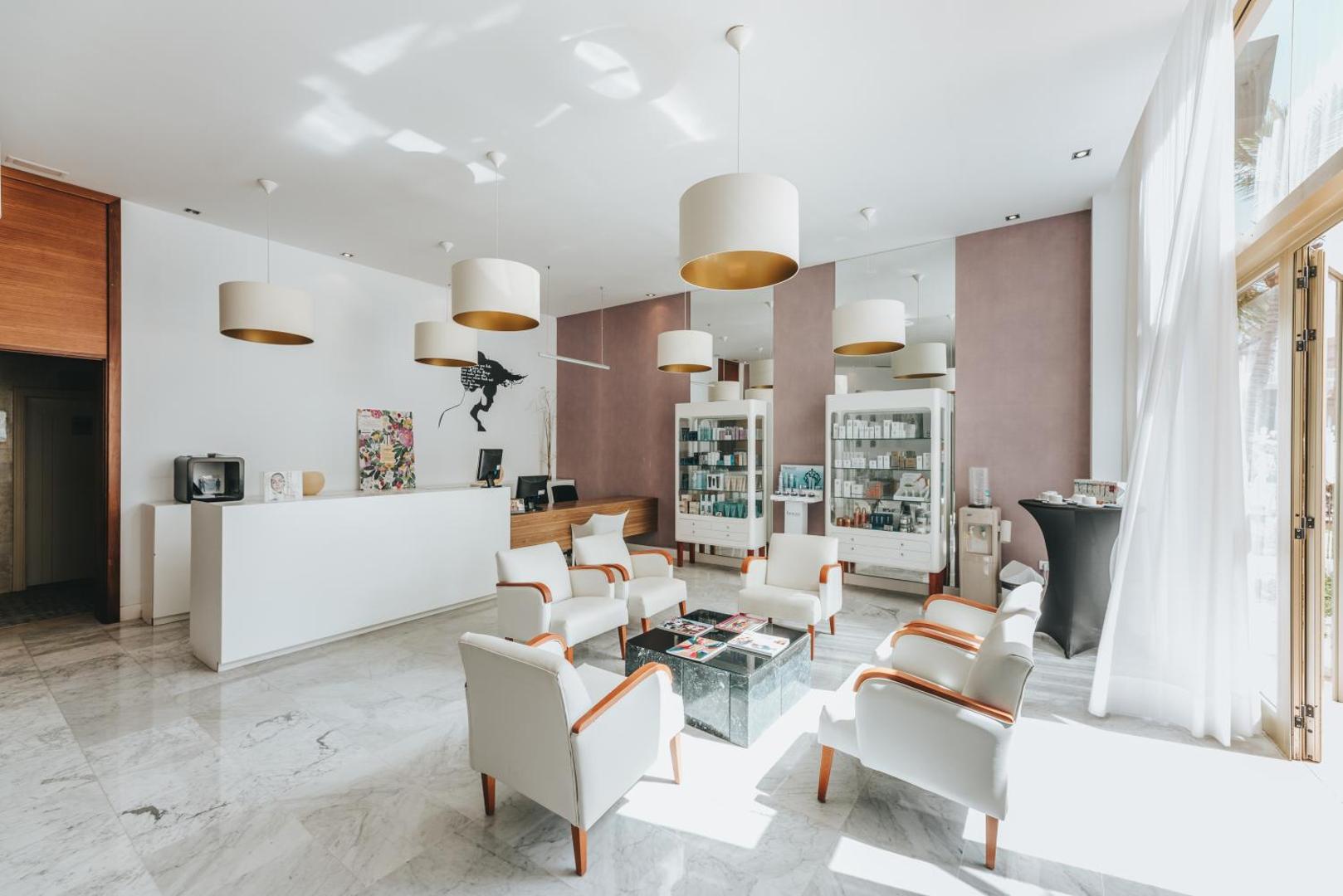 Gaiša un moderna Cleopatra Palace spa recepcijas zona ar baltiem atpūtas krēsliem, marmora grīdu un kosmētikas vitrīnām