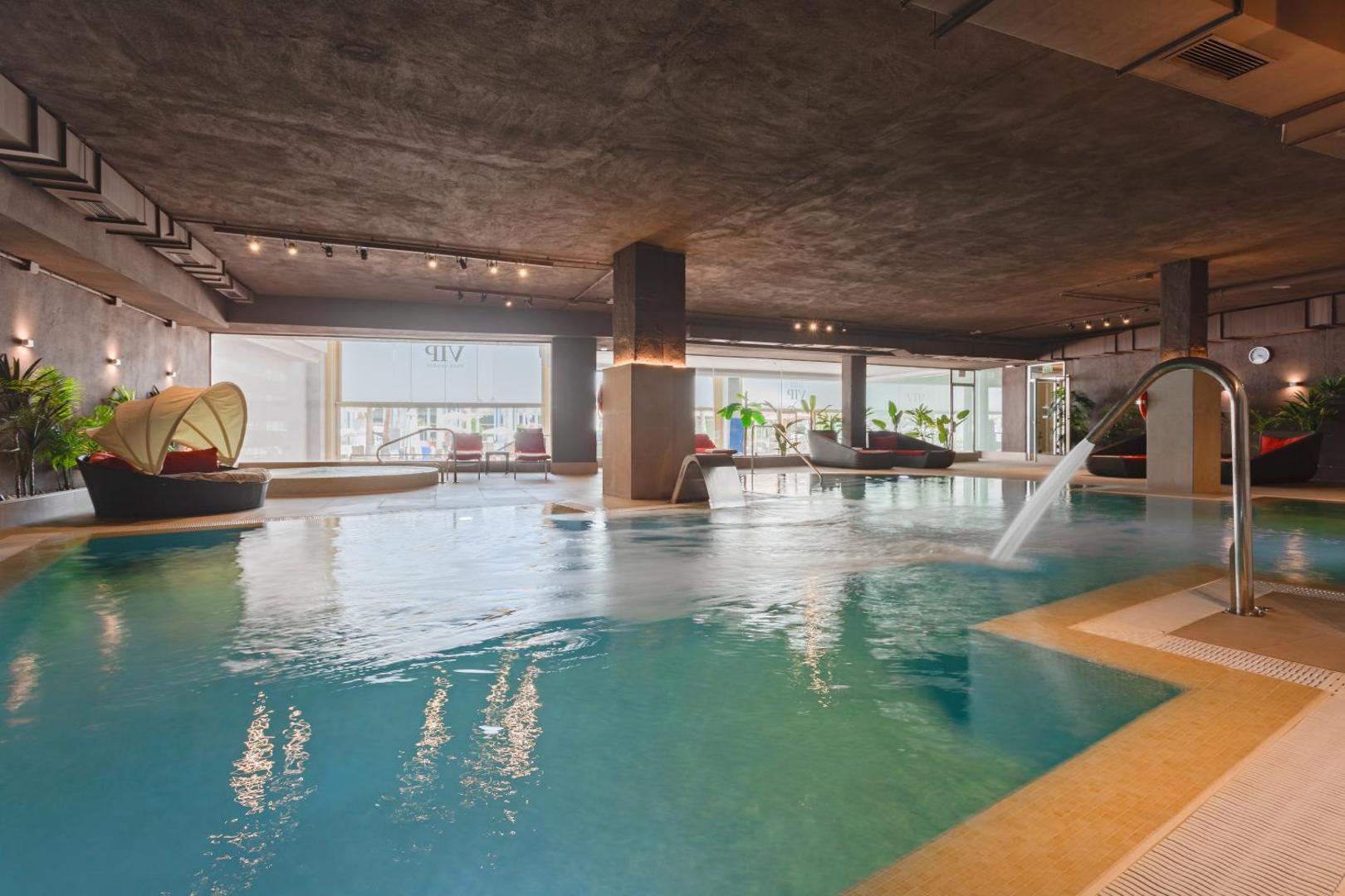 Cleopatra Palace iekštelpu spa baseins ar kaskādēm, masāžas strūklām un atpūtas krēsliem modernā, industriālā stila interjerā