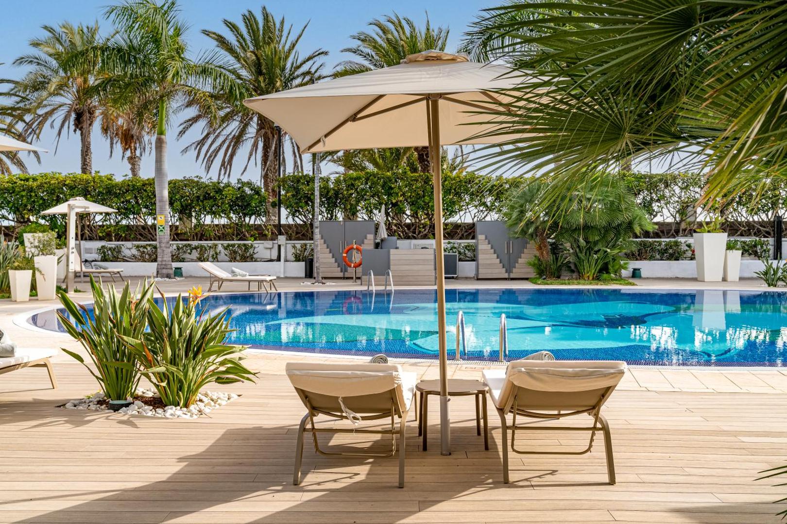 Sir Anthony Hotel āra baseins ar zviļņiem un saulessargiem Tenerifē, apkārtnē augošas palmas un tropu dārzs