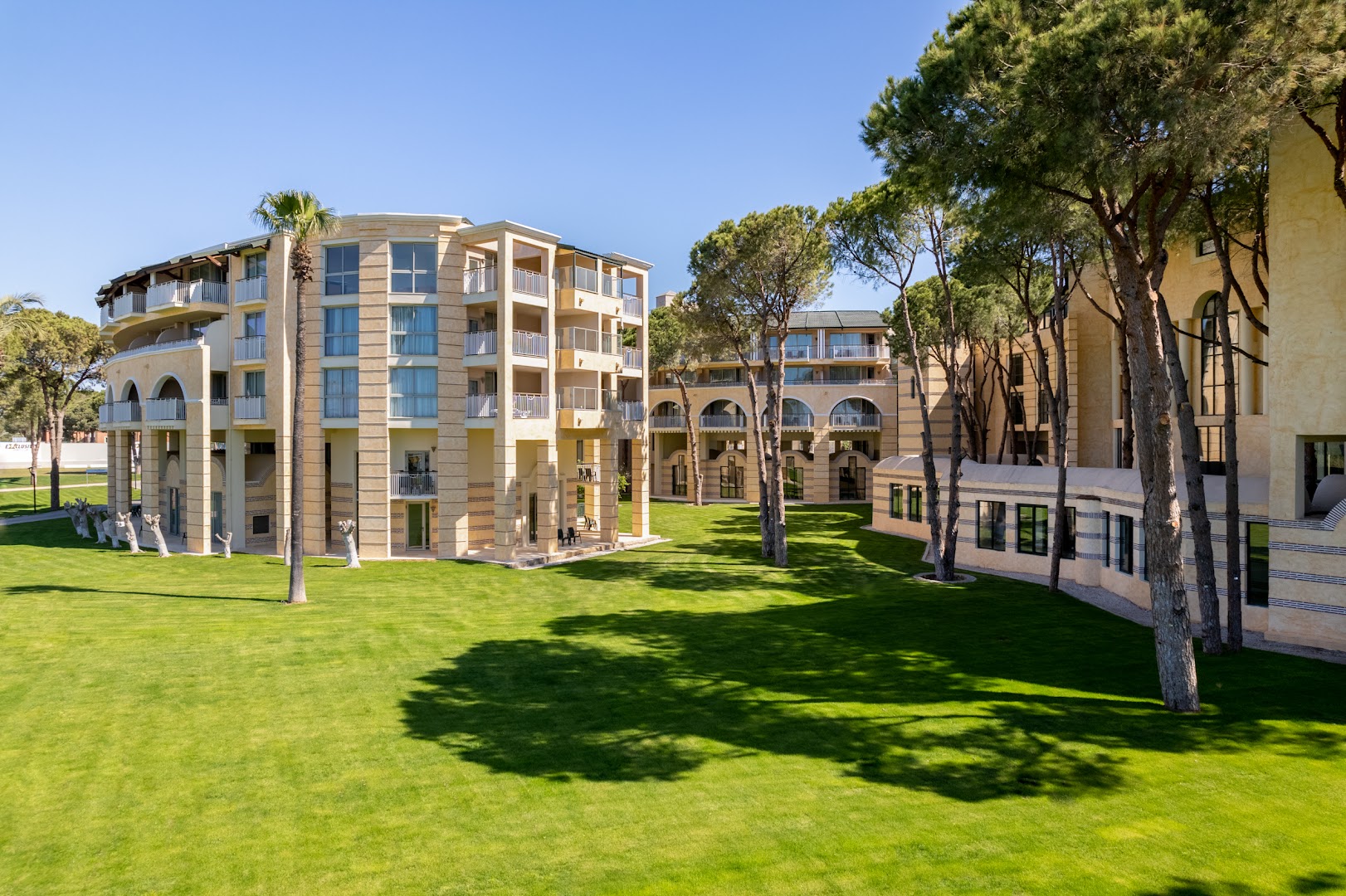 Rixos Park Belek modernā arhitektūra ar gaišām fasādēm, plašiem zālieniem un priedēm Belekas kūrortā