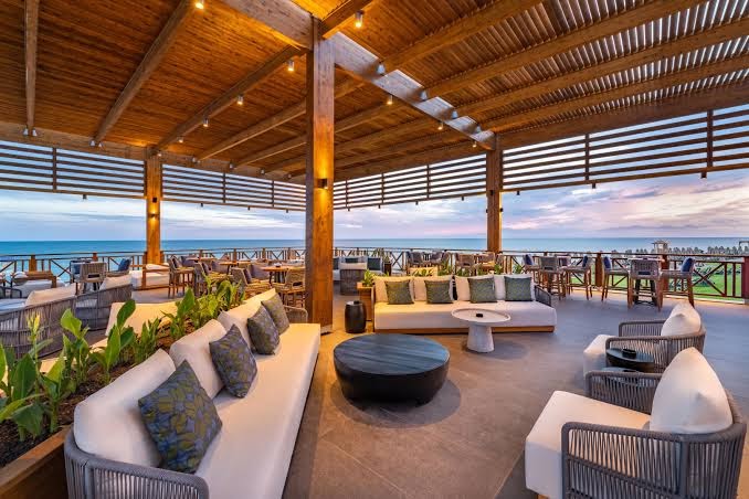 Rixos Park Belek āra terases bārs ar koka konstrukcijām, mīkstiem dīvāniem un skatu uz jūru saulrieta laikā