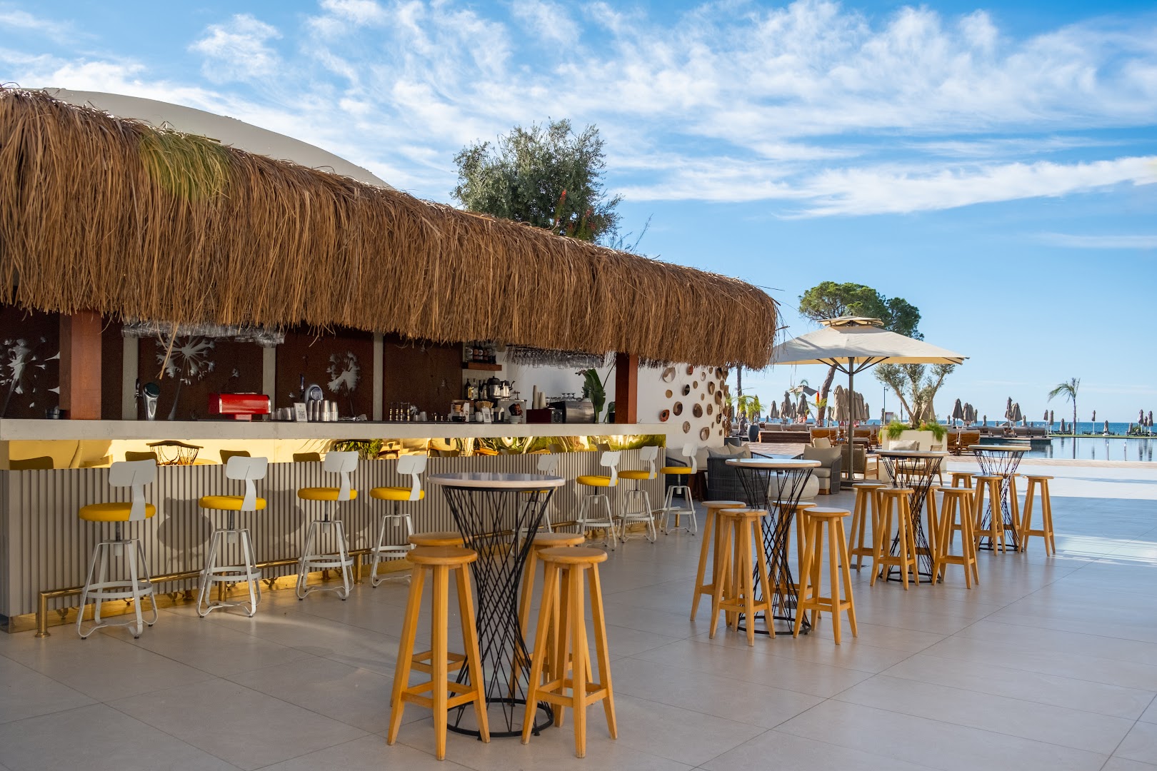 Rixos Park Belek pludmales bārs ar augstajiem krēsliem, salmu jumtu un skatu uz jūru un baseina zonu