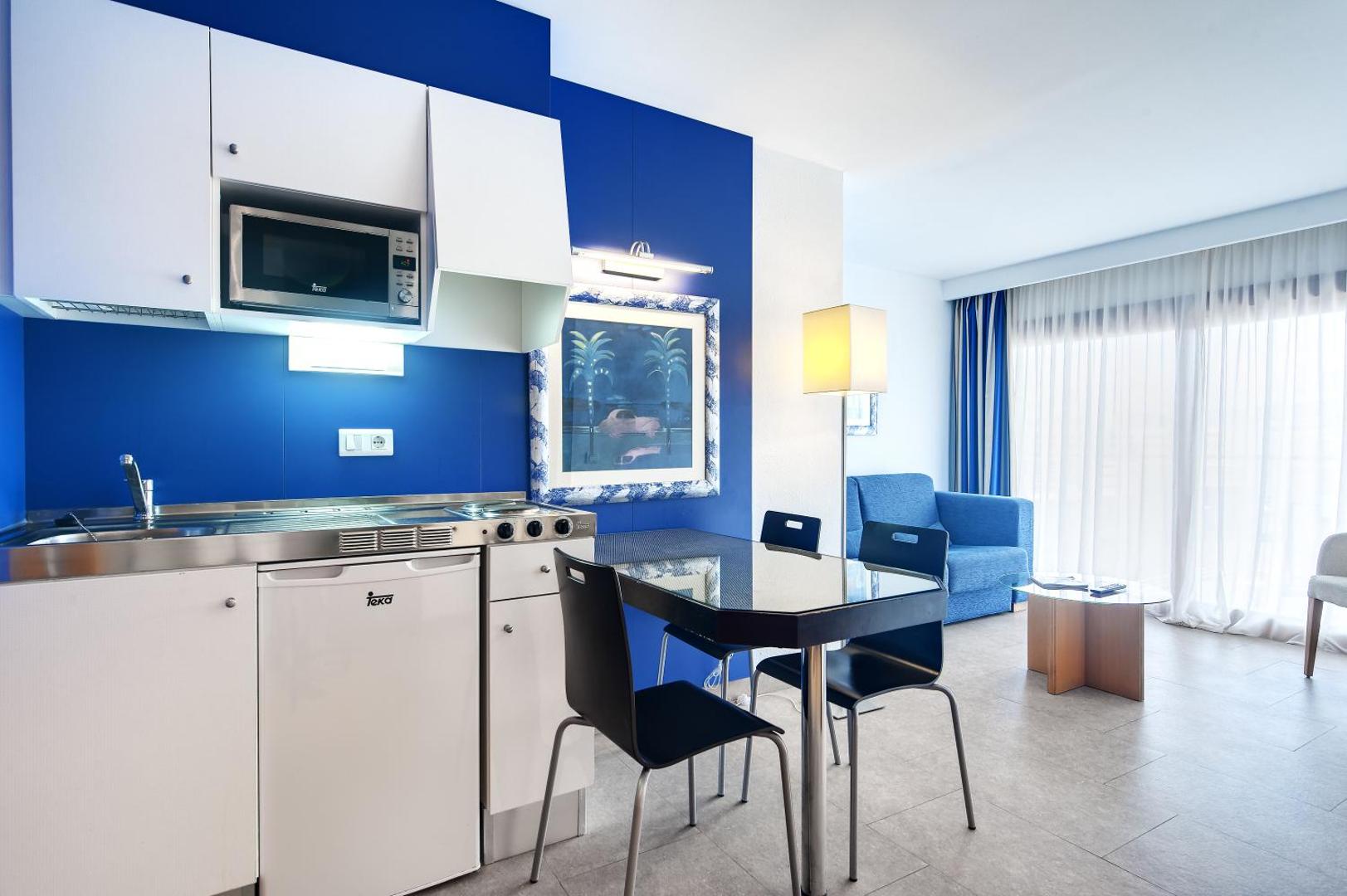Barcelo Margaritas apartamentu virtuves zona ar mikroviļņu krāsni, ledusskapi, pusdienu galdu un zilu akcenta sienu