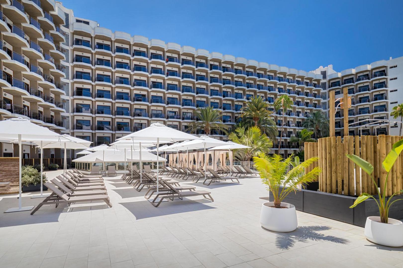 Barceló Margaritas viesnīcas sauļošanās terase Grankanārijā ar gaišām flīzēm, daudziem zviļņiem, saulessargiem un skatu uz daudzstāvu korpusu