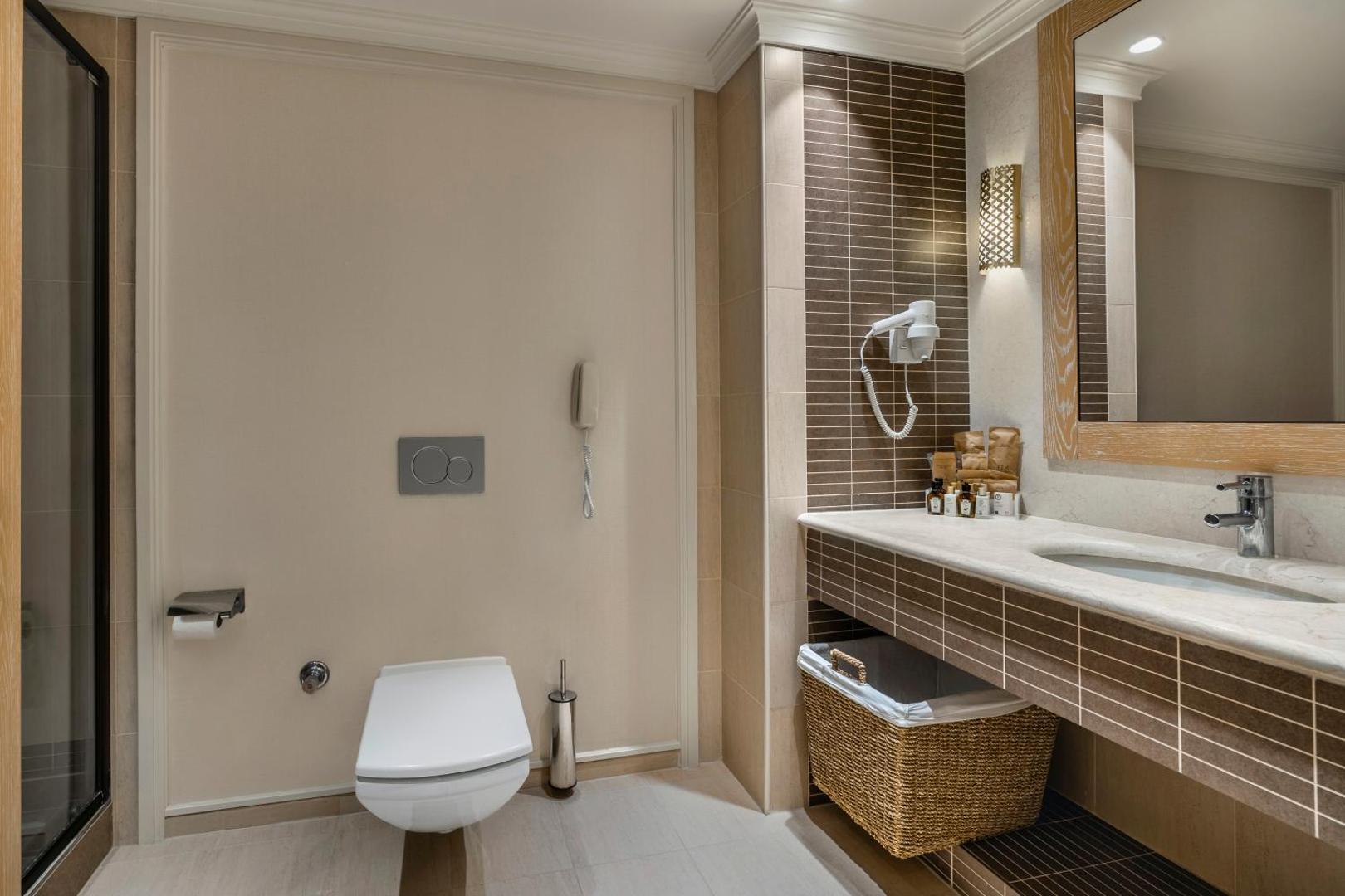 Ela Excellence Resort Belek numura vannas istaba ar modernu santehniku, dušu, izlietni un pītu veļas grozu — gaišs un tīrs dizains