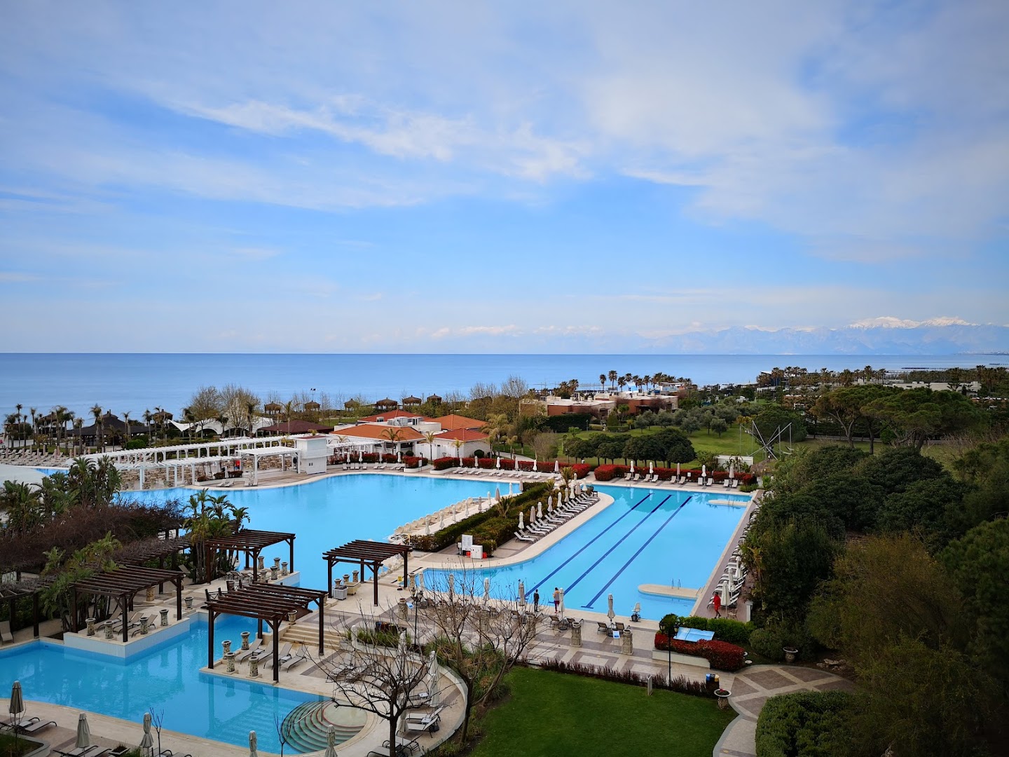 Ela Excellence Resort Belek teritorijas skats uz baseiniem un Vidusjūras piekrasti ar kalniem fonā skaidrā dienā