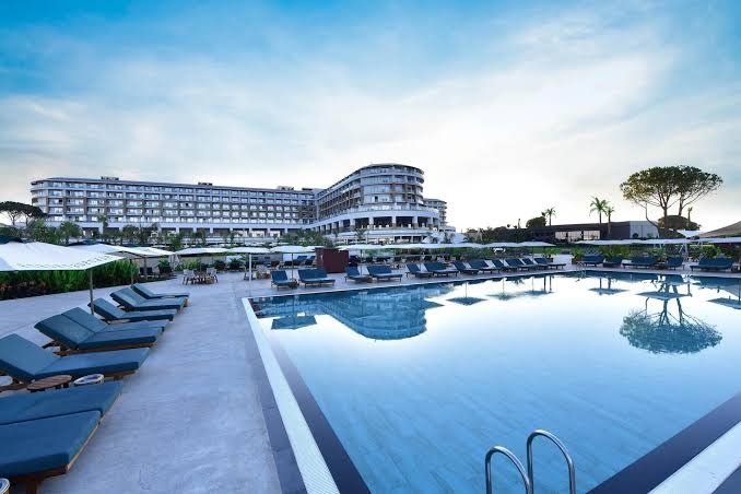 Ethno Belek galvenais āra baseins ar ziliem sauļošanās krēsliem un skatu uz moderno viesnīcas ēku Belekā, Turcijā