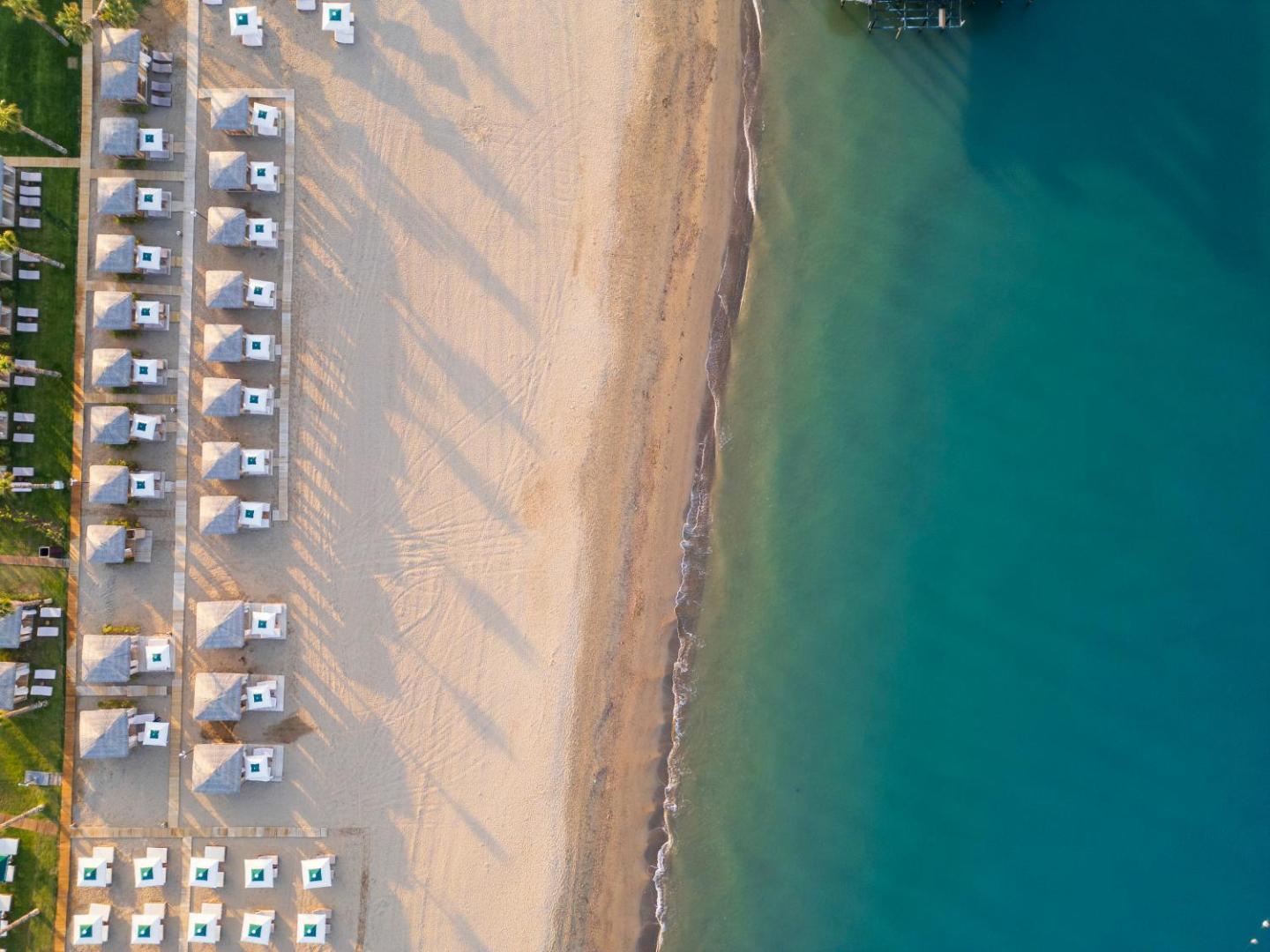 Ethno Belek viesnīcas pludmales skats no putna lidojuma, smilšu josla, tirkīza ūdens un sakārtotas atpūtas zonas ar saulessargiem