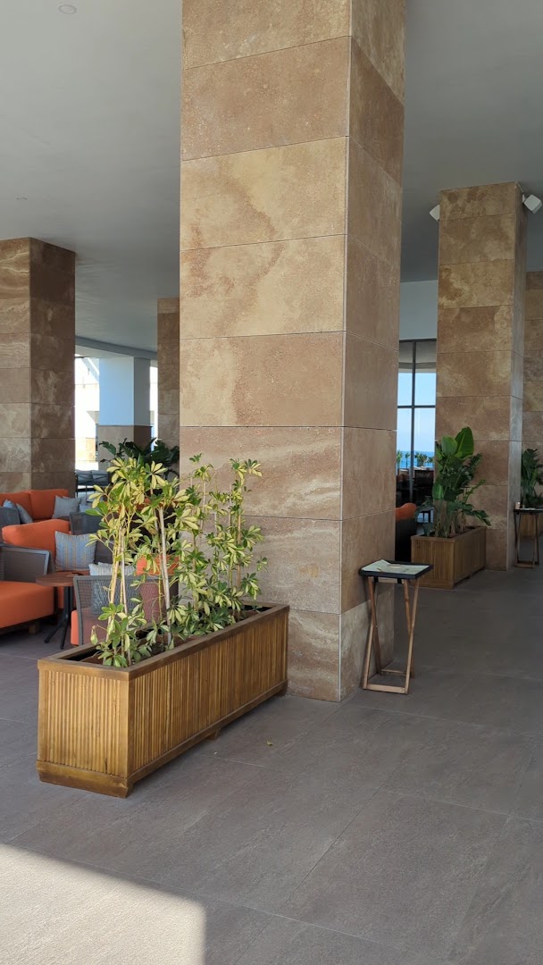 Ethno Belek viesnīcas lobby atpūtas zona ar masīvām akmens kolonnām, oranžiem dīvāniem un zaļiem augiem podos