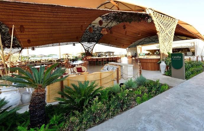 Ethno Belek viesnīcas Casita bārs un atpūtas zona zem liela nojumes jumta piekrastē — mīkstie dīvāni, palmas un skats uz jūru
