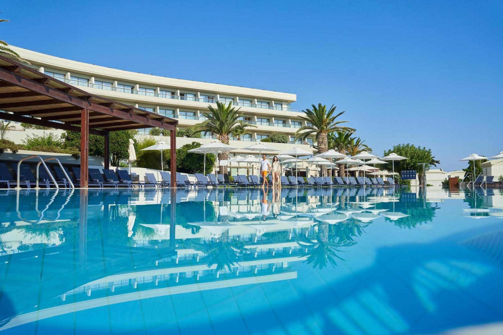 Agapi Beach Resort lielais āra baseins ar dzidru ūdeni, sauļošanās krēsliem un viesnīcas ēku fonā Amudarā, Krētā