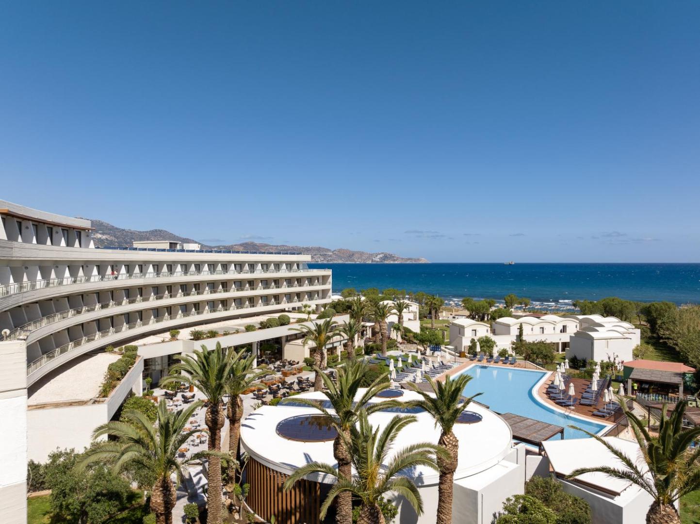 Agapi Beach Resort panorāmas skats uz galveno ēku, baseinu un jūru Krētā — plaša teritorija ar palmām un sauļošanās zonu