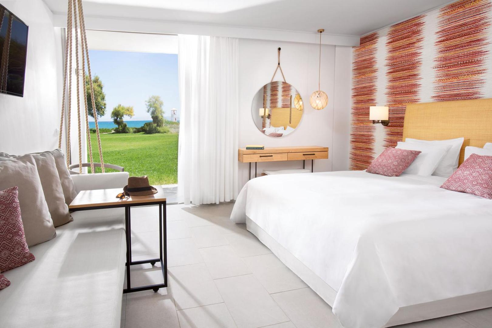 Agapi Beach Resort gaišs numurs ar modernu dizainu un izeju uz dārzu — balta gulta, dekoratīvi elementi un skats uz jūru