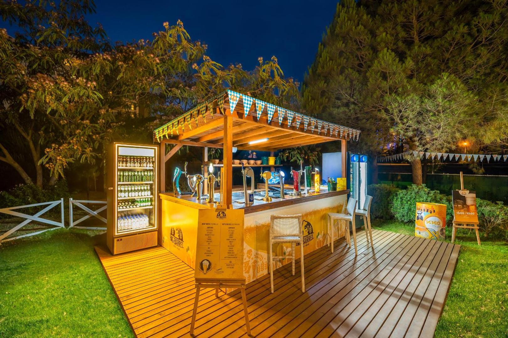 Concorde De Luxe Resort dārza bārs vakarā ar izgaismotu koka terasi un mājīgu apgaismojumu starp zaļojošiem kokiem