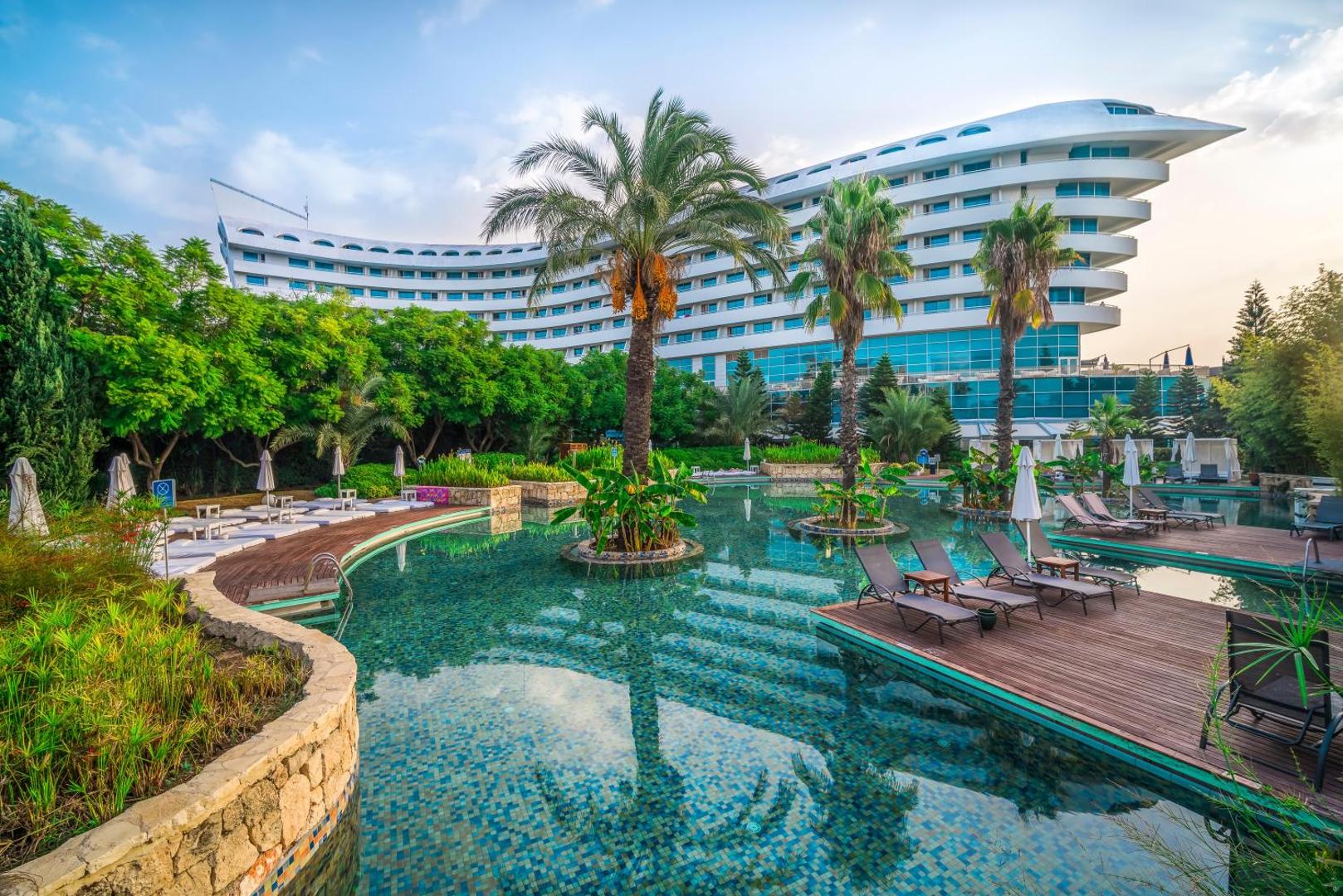 Concorde De Luxe Resort eksotisks baseins ar koka terasēm un sauļošanās krēsliem Antaljā — palmas un viesnīcas arhitektūra