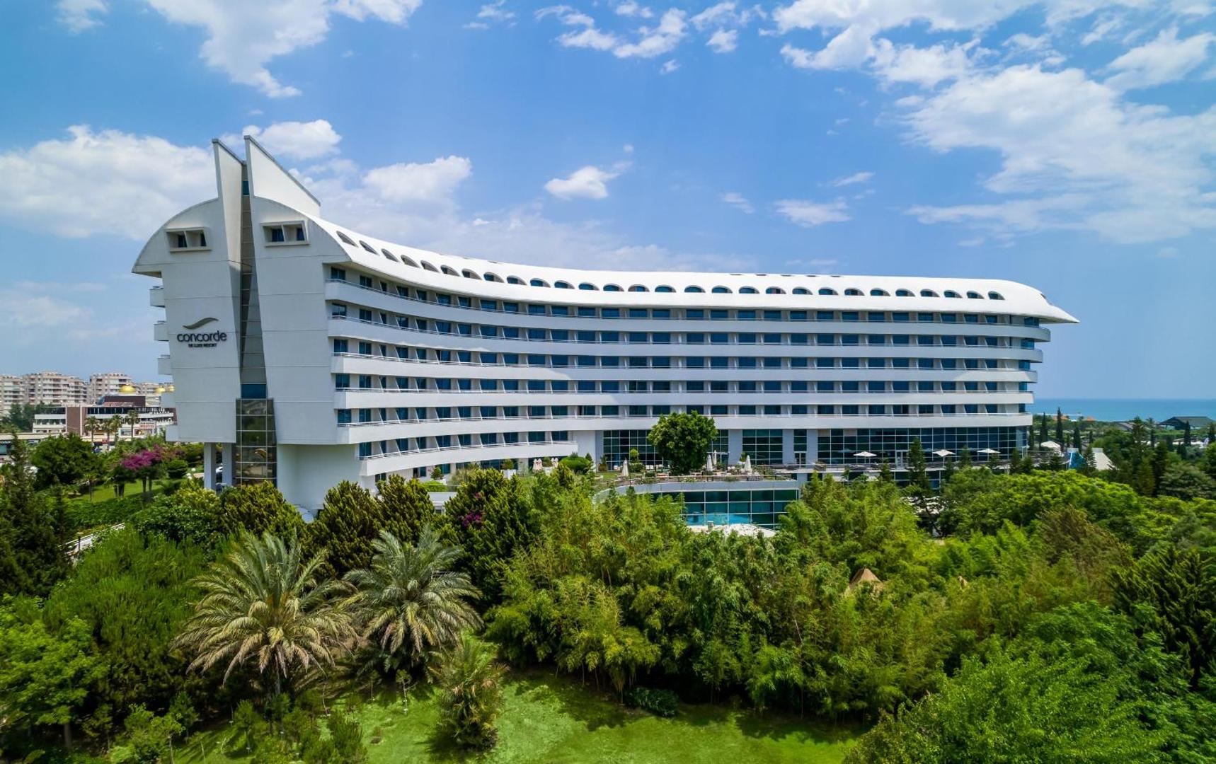 Viesnīcas Concorde De Luxe Resort modernā arhitektūra Antaljā, Turcijā — balta ēka lidmašīnas formā, ko ieskauj kupls palmu dārzs