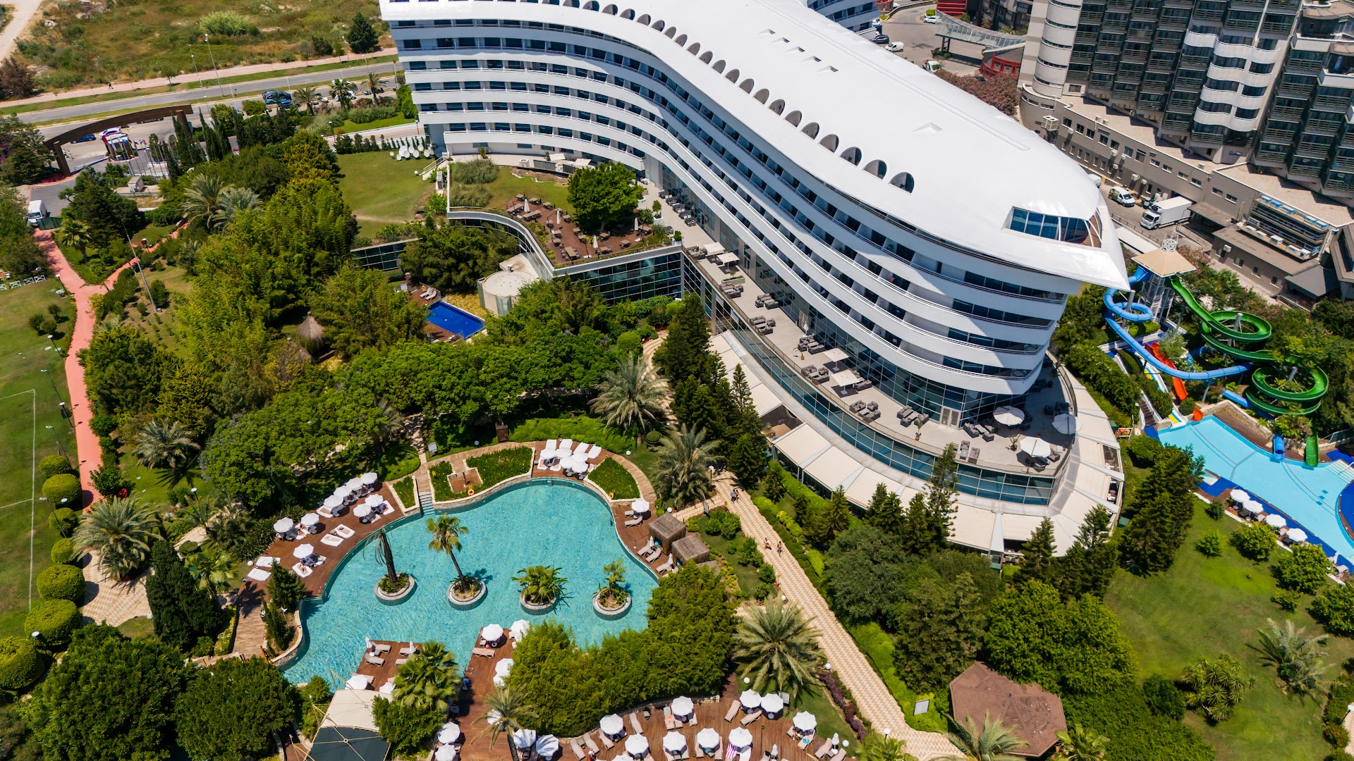 Aerofoto skats uz Concorde De Luxe Resort baseinu zonu un akvaparku — atpūtas krēsli, palmas un zili baseini pie viesnīcas korpusa