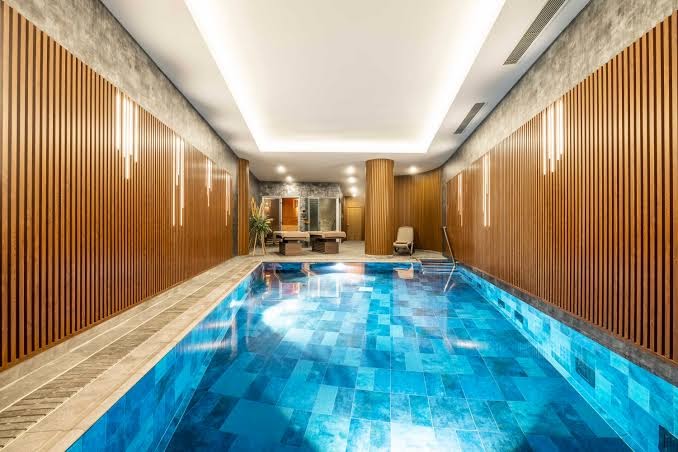 Concorde De Luxe Resort iekštelpu baseins ar zilu flīžu apdari, koka paneļu sienām un atpūtas krēsliem spa zonā