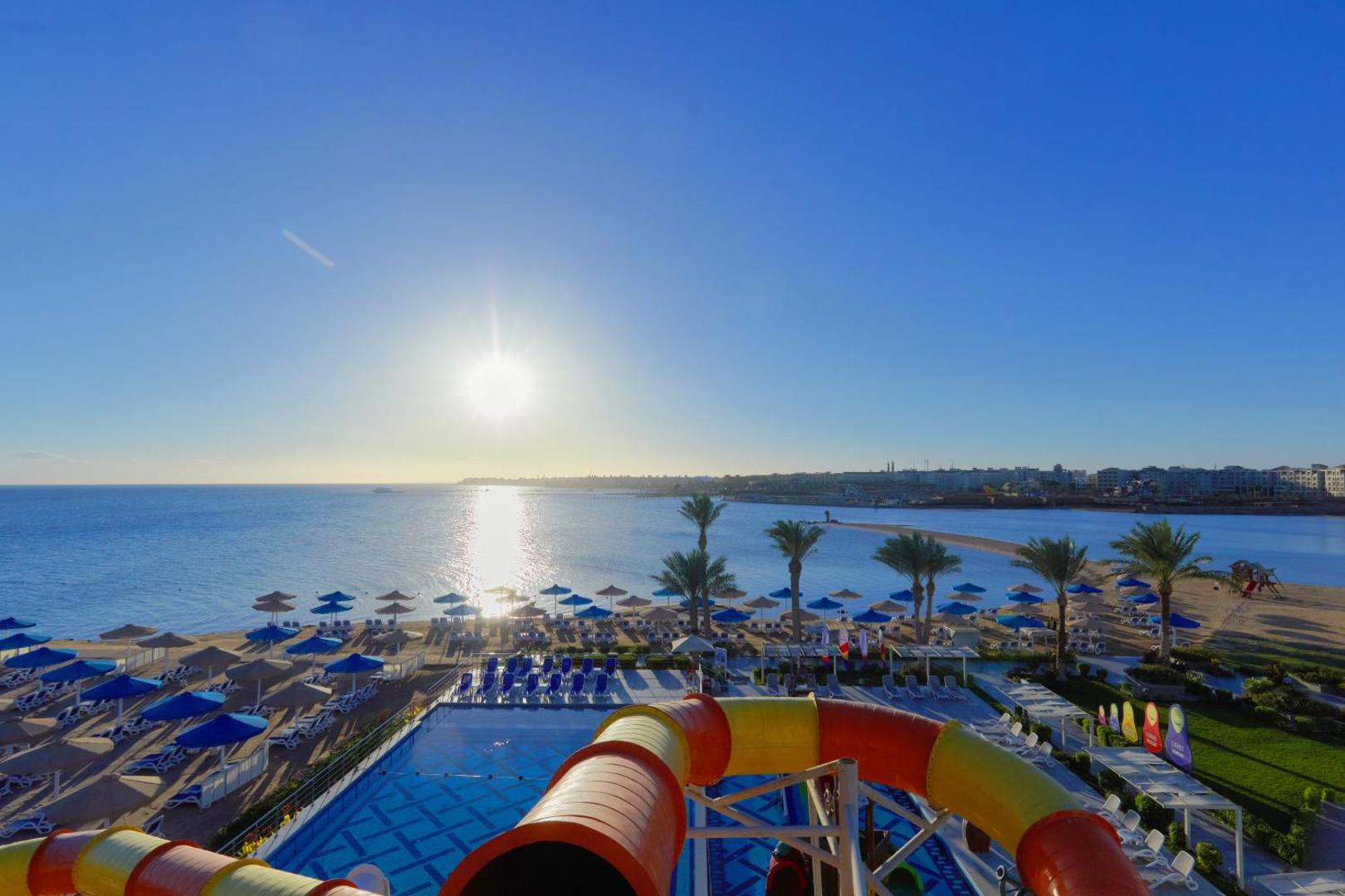 Skats no Bellagio Beach Resort & Spa ūdens slidkalniņa uz pludmali, saulaino piekrasti un baseina zonu Hurgadā