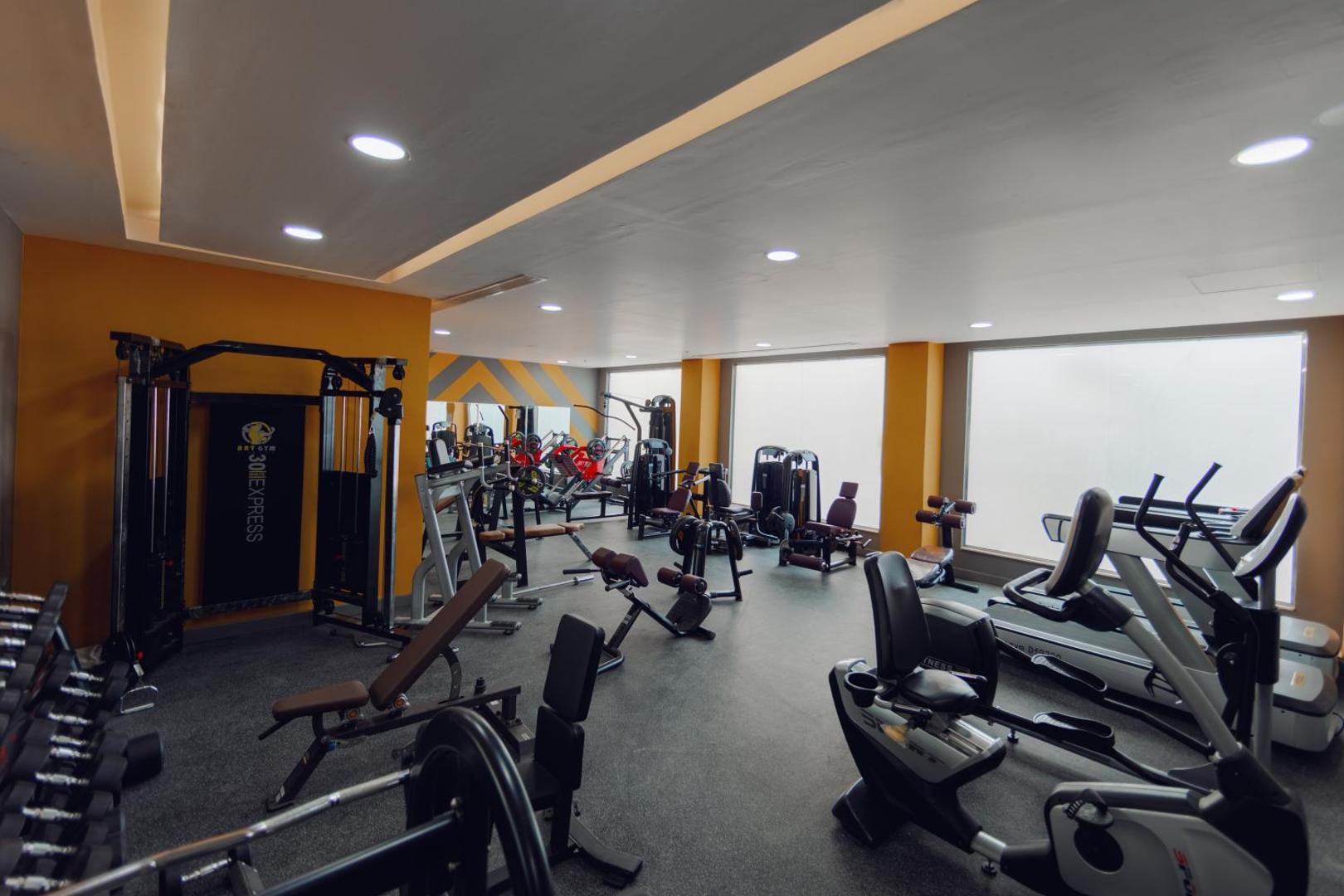 Bellagio Beach Resort & Spa moderns fitnesa centrs ar trenažieriem, skrejceļiem un brīvajiem svariem gaišā telpā ar lieliem logiem.