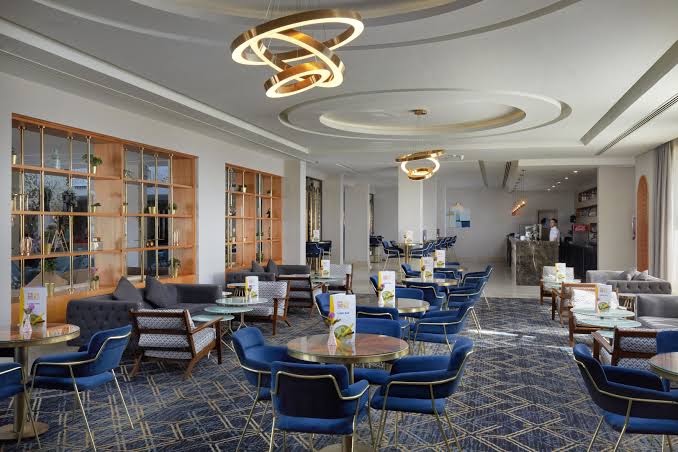 Bellagio Beach Resort & Spa lobby bārs ar modernām mēbelēm, ziliem krēsliem un dizaina apgaismojumu — vieta kokteiļiem un atpūtai
