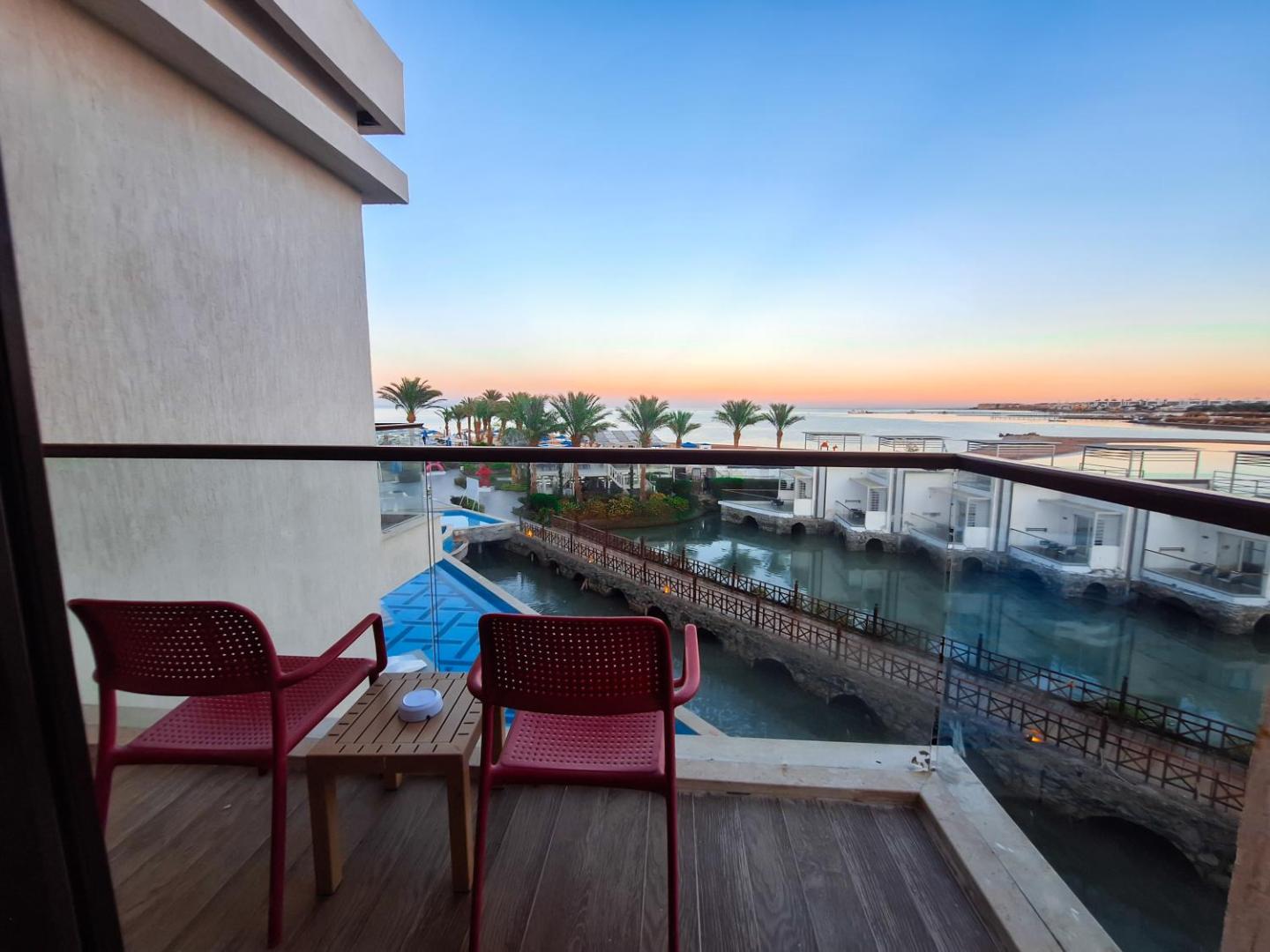 Bellagio Beach Resort & Spa numura balkons ar skatu uz lagūnu un palmu dārzu saulrietā Hurgadā, Ēģiptē