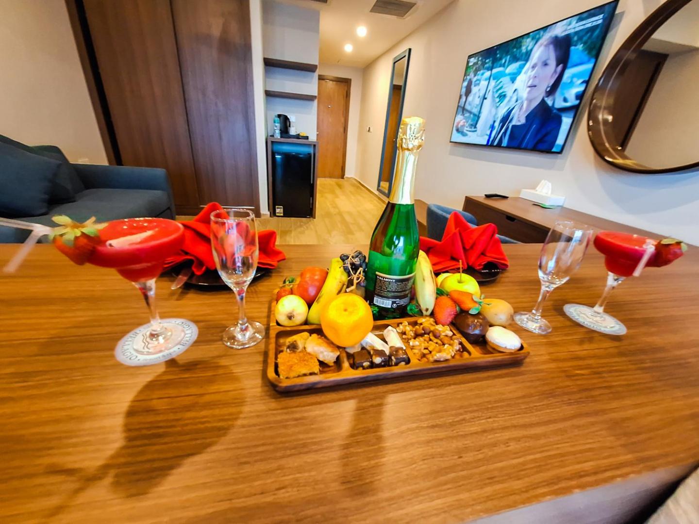 Bellagio Beach Resort & Spa viesnīcas numurs ar sagaidīšanas paplāti — augļi, saldumi, dzirkstošais vīns un kokteiļi uz koka virsmas.