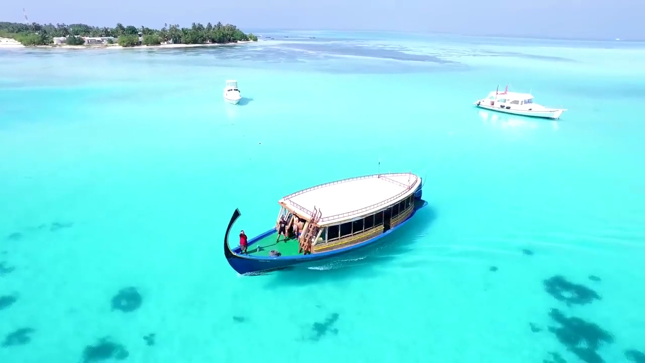 Tradicionāla laiva tirkīzzilā okeāna ūdenī pie Sheraton Maldives Full Moon Resort & Spa salas krastiem