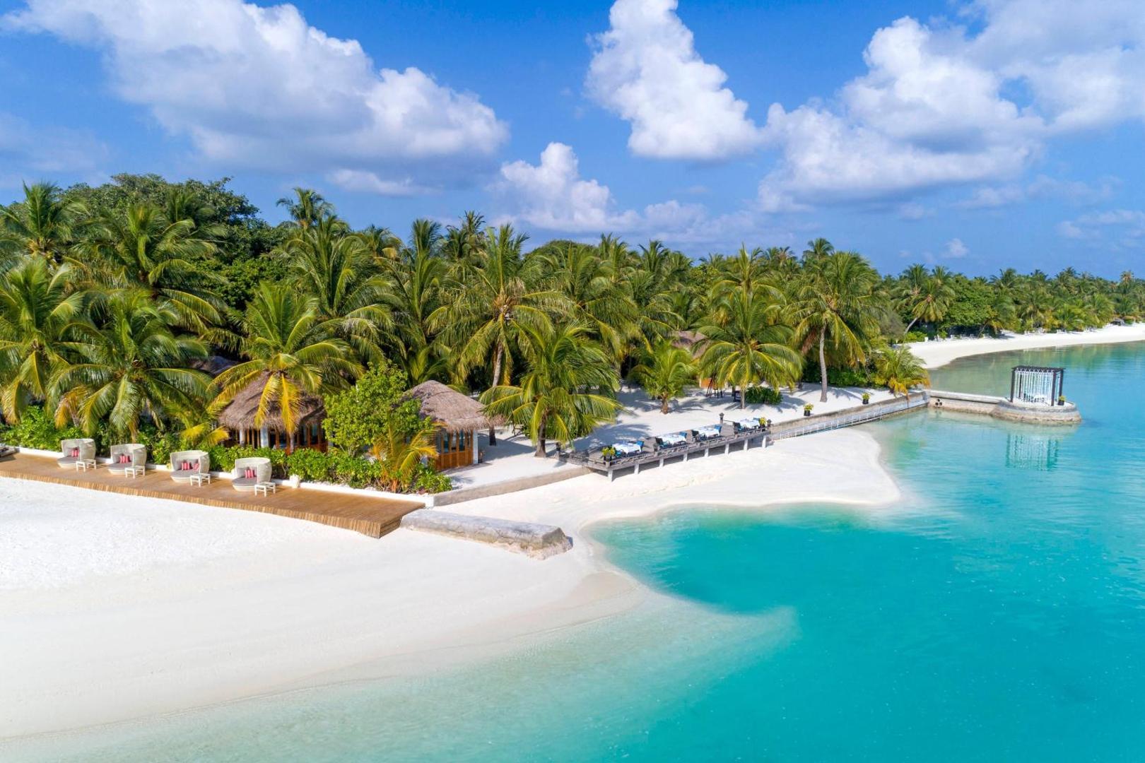 Sheraton Maldives Full Moon Resort & Spa pludmales restorāns un sauļošanās krēsli zem palmām pie tirkīza lagūnas