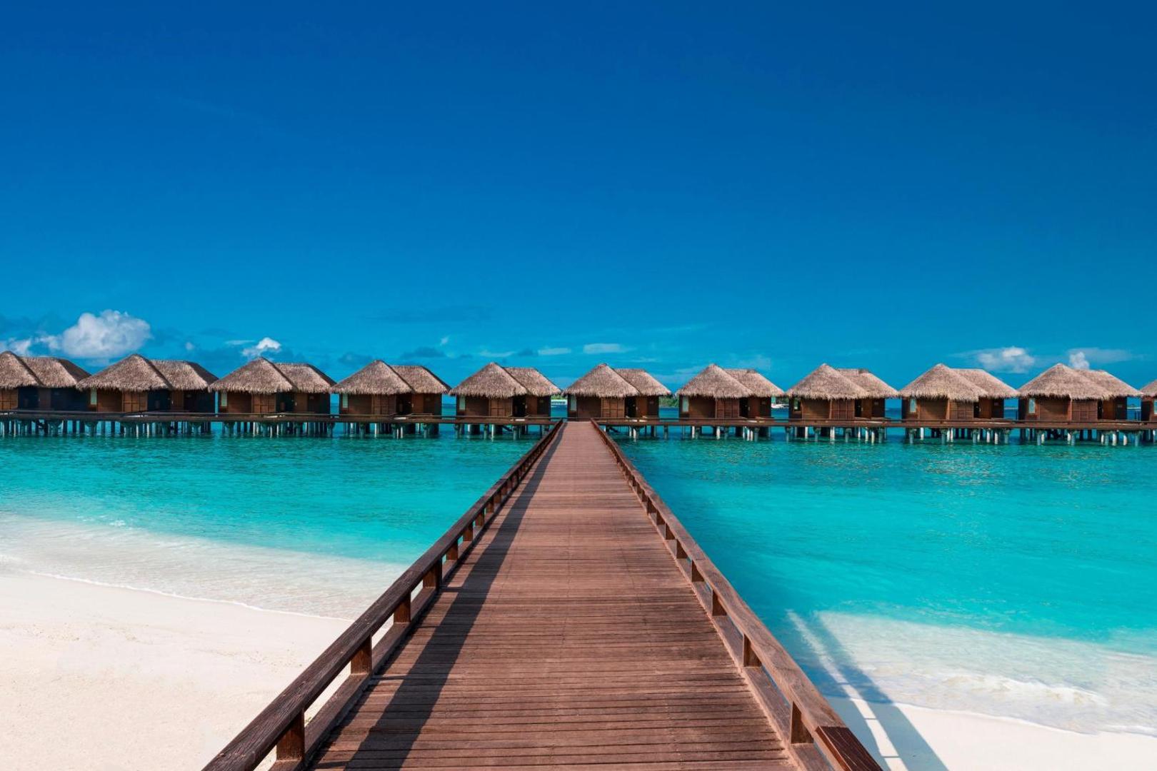 Koka laipa uz Sheraton Maldives Full Moon Resort & Spa ūdens bungalo pie balto smilšu pludmales zem skaidrām debesīm