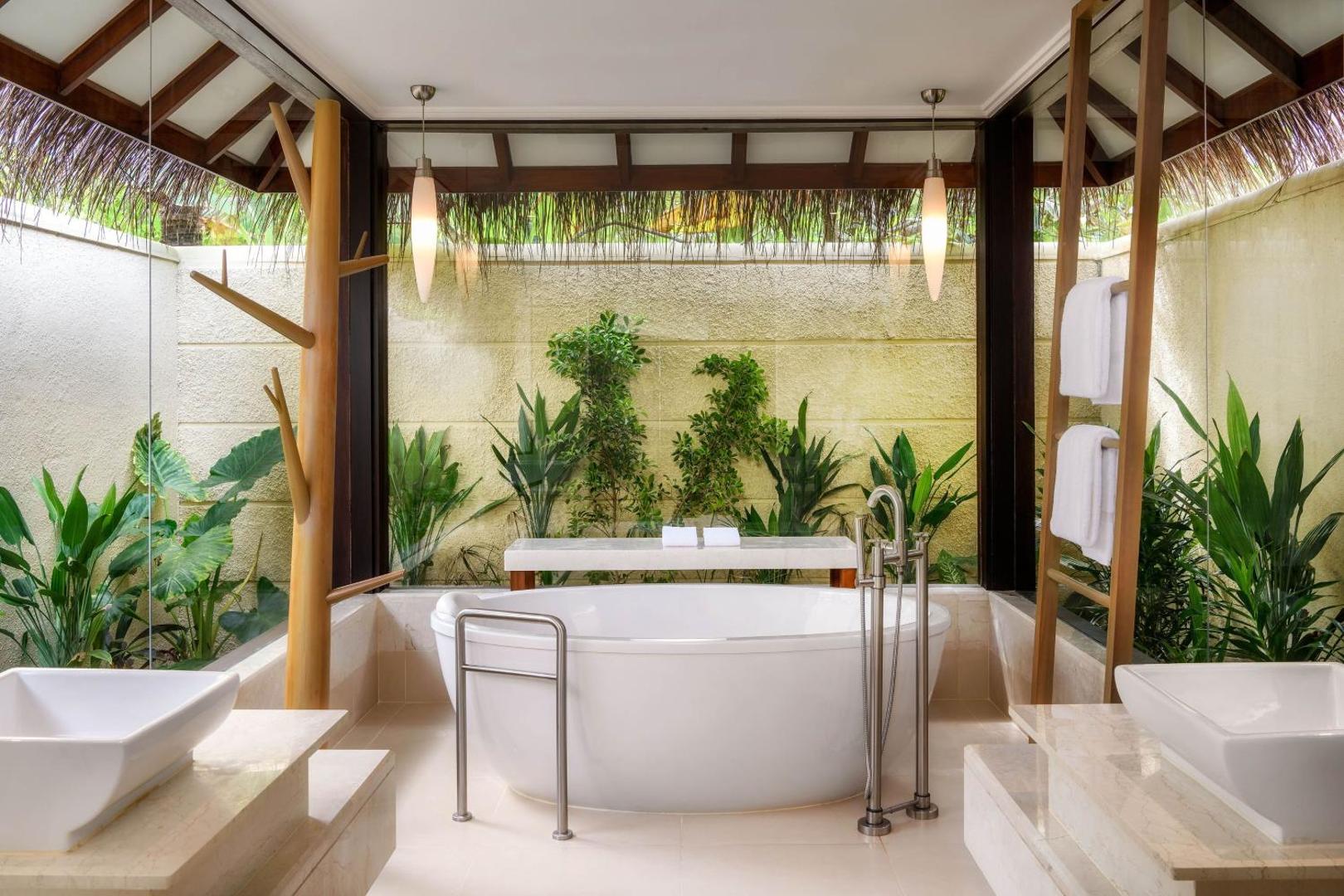 Sheraton Maldives Full Moon Resort & Spa vannas istaba ar brīvstāvošu vannu, tropu augiem un dabisku apgaismojumu villas iekšpagalmā