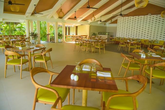 Sheraton Maldives Full Moon Resort & Spa restorāna iekštelpas ar koka galdiem un dzelteniem krēsliem gaišā un plašā telpā