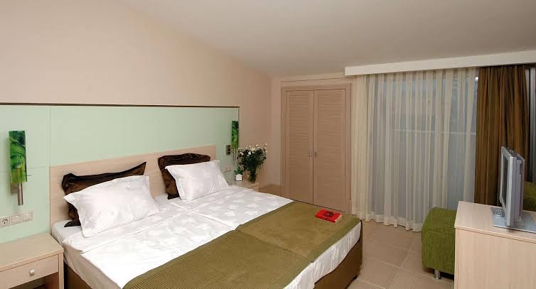 Ambassador Plaza Hotel gaišs viesnīcas numurs ar divguļamo gultu, koka mēbelēm, televizoru un izeju uz balkonu