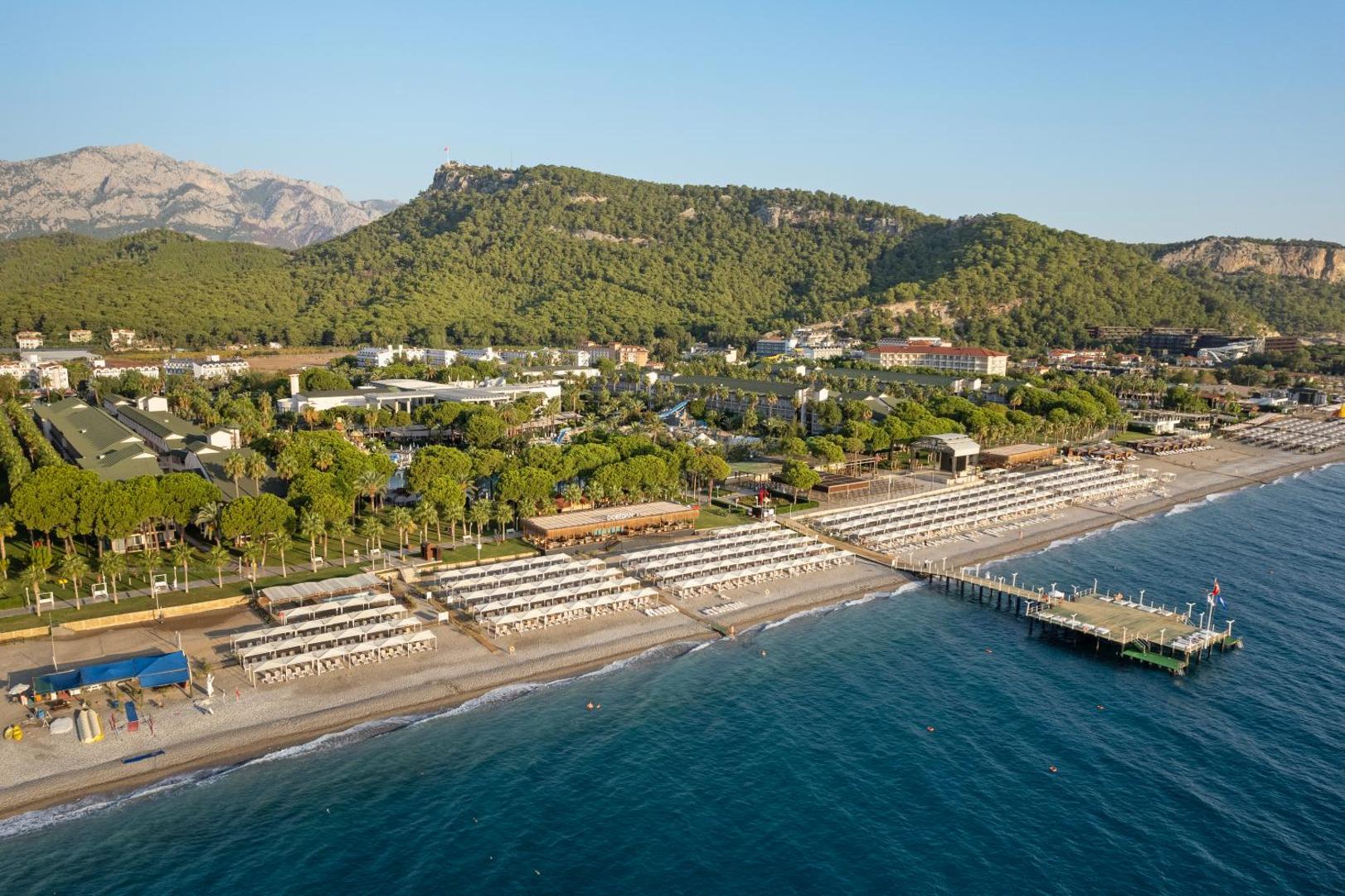 Dobedan World Palace viesnīcas panorāma ar kalniem fonā un plašo oļu pludmali — skats uz piekrasti un piestātni