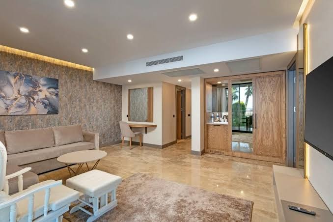 Dobedan World Palace plaša viesistabas zona ar dīvānu, atpūtas krēsliem un marmora grīdu viesnīcas numurā Antaljas piekrastē