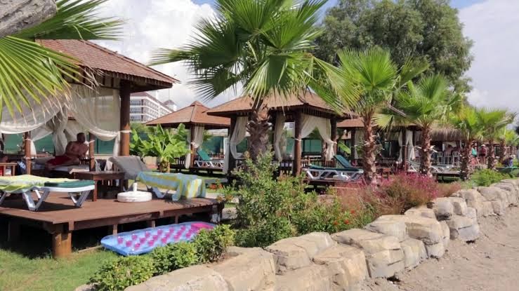 Eftalia Splash Resort pludmales bungalo un atpūtas krēsli palmu ieskautā dārzā pie smilšu pludmales Alānijā