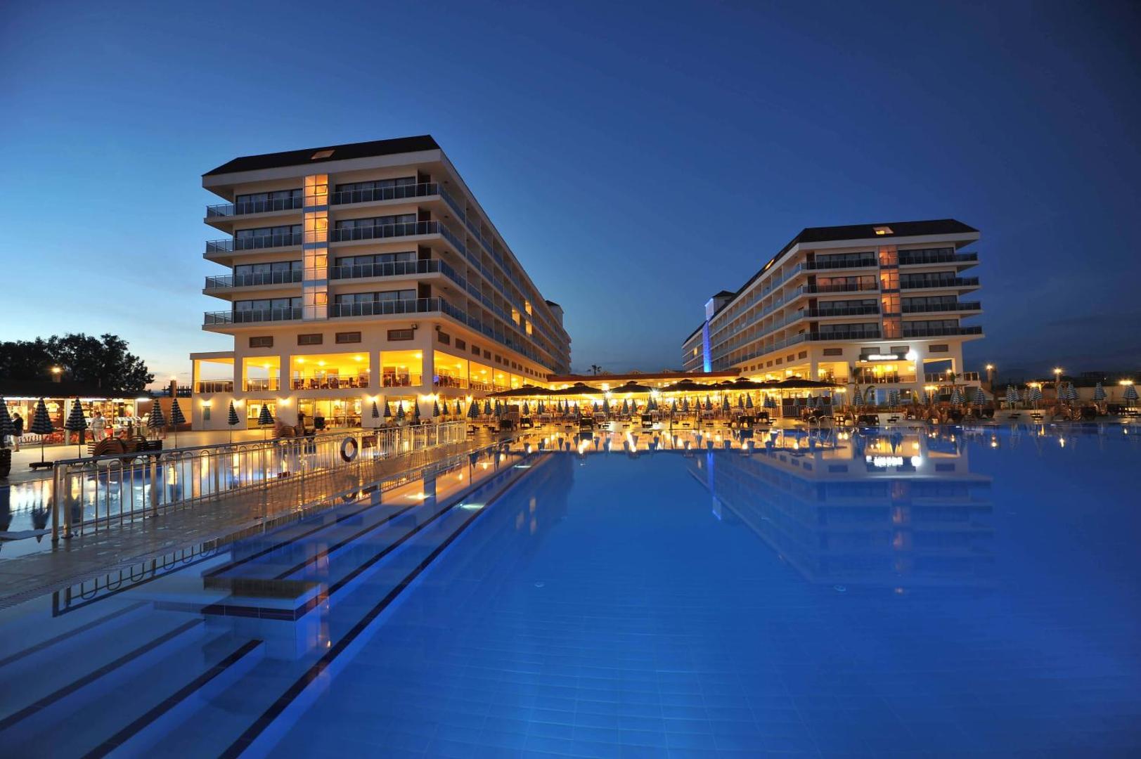 Eftalia Splash Resort viesnīcas korpusi un baseina zona vakara apgaismojumā Alānijā — izgaismotas terases un mierīga atmosfēra