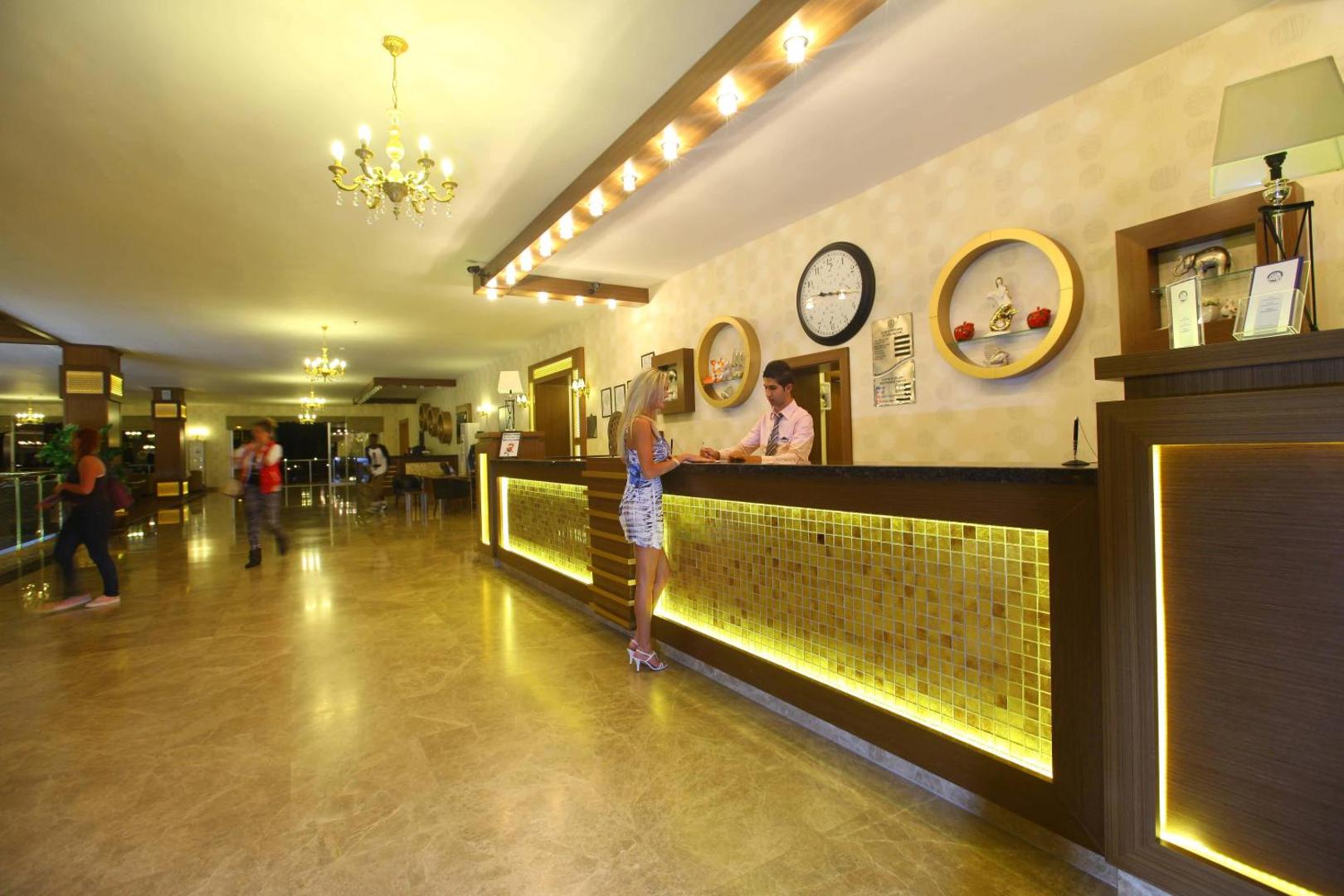 Viesnīcas Eftalia Splash Resort recepcijas lete ar apgaismojumu un personālu, kas apkalpo viesi modernā interjerā