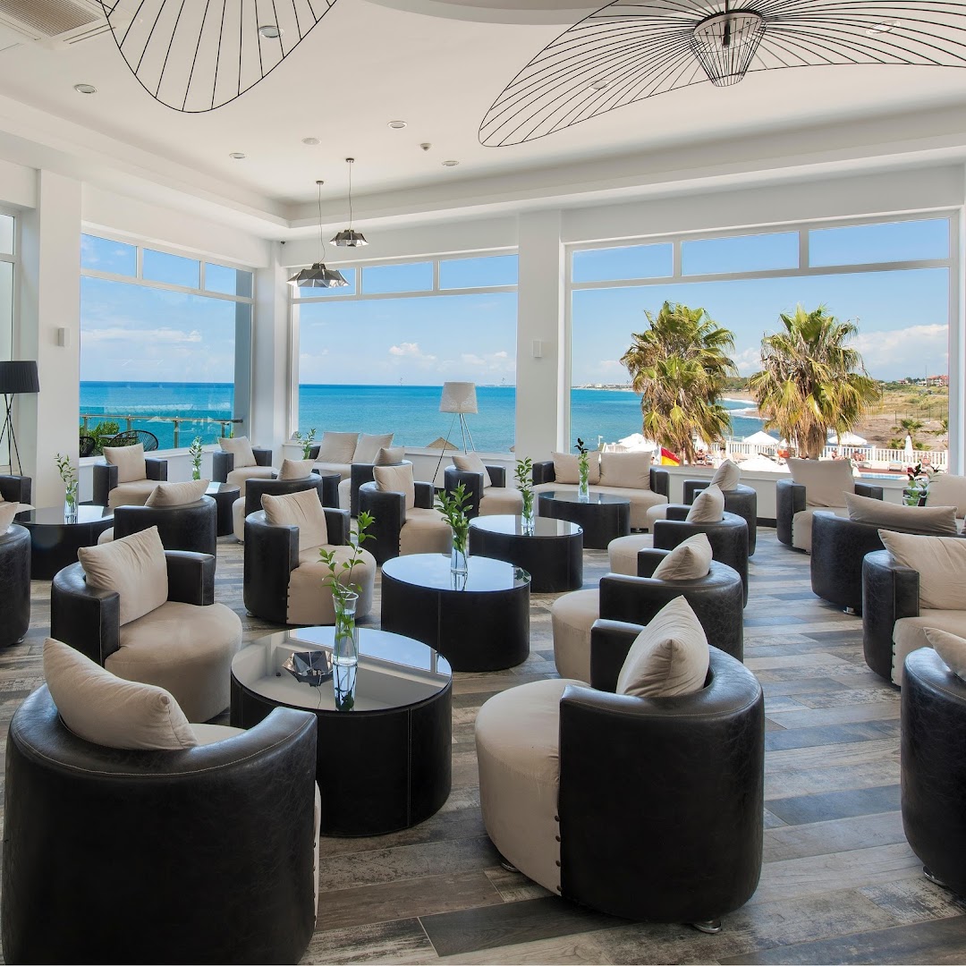 Flora Garden Beach viesnīcas lobby bārs ar moderniem atpūtas krēsliem un lieliem logiem, no kuriem paveras skats uz jūru
