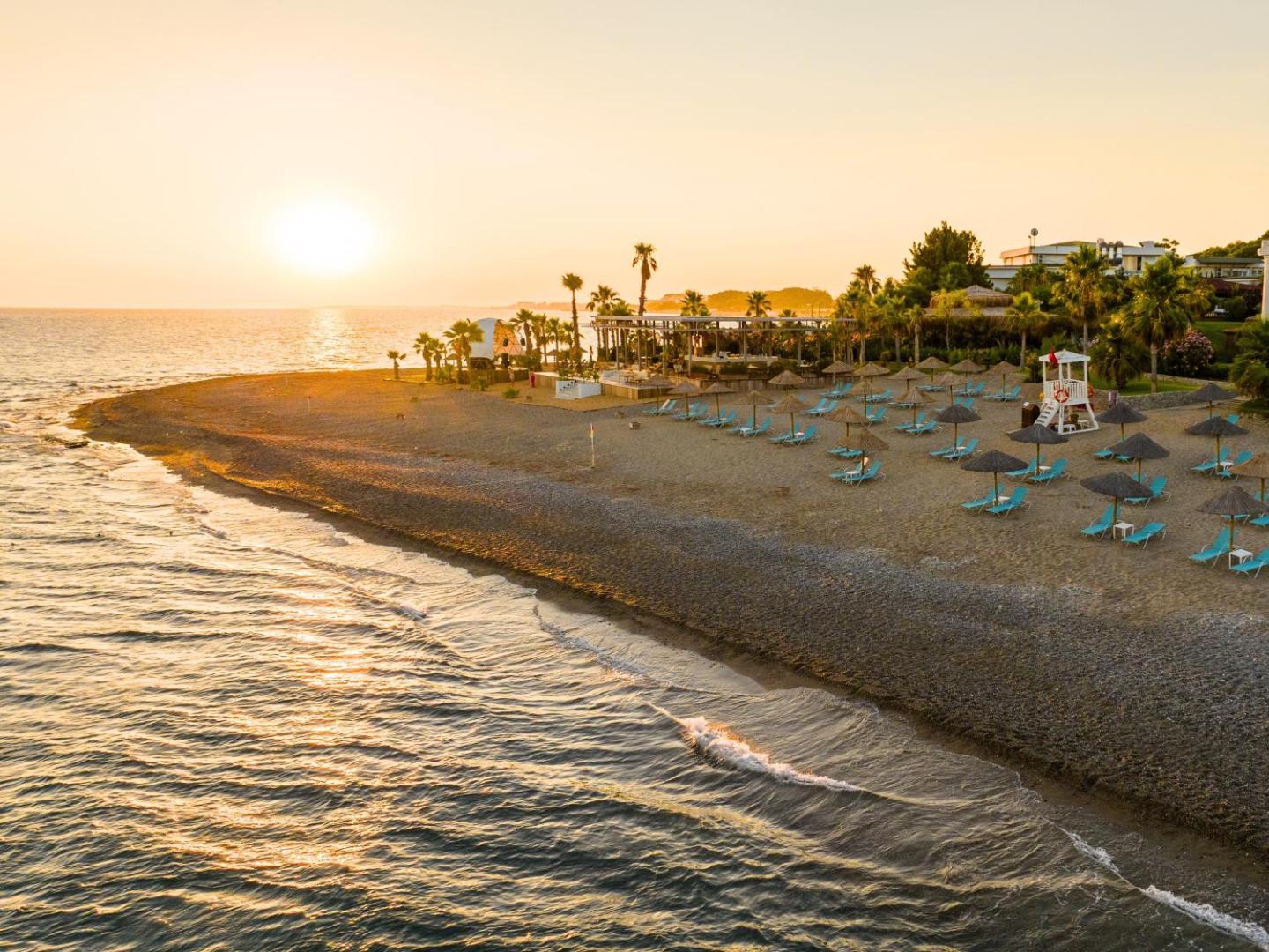 Flora Garden Beach viesnīcas privātā pludmale saulrieta laikā Turcijā — smilšu un oļu krasts ar saulessargiem un jūras skatu