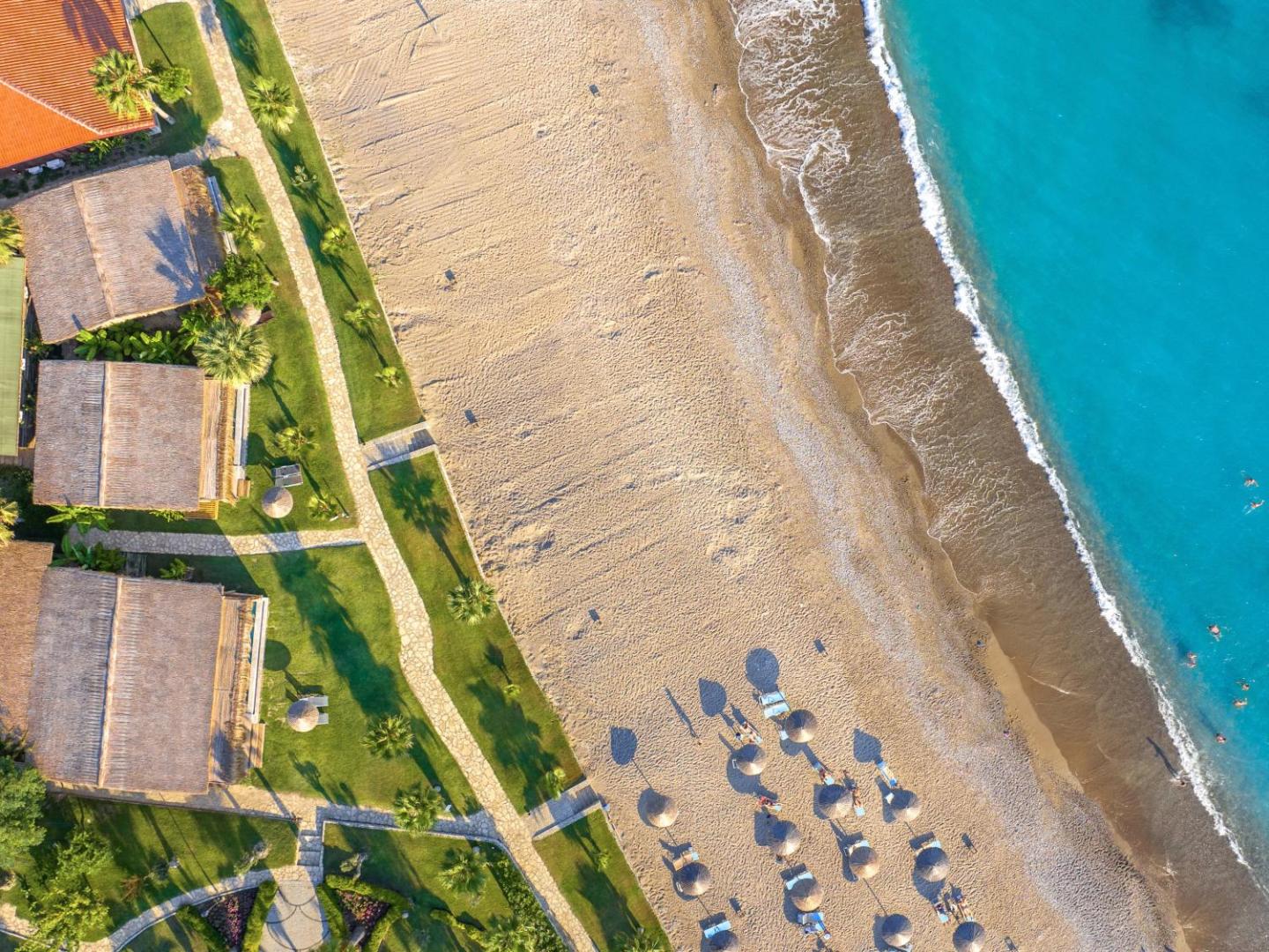 Flora Garden Beach bungalo un pludmales zona no augšas — zaļš mauriņš, palmas un smilšu krasts pie tirkīza jūras