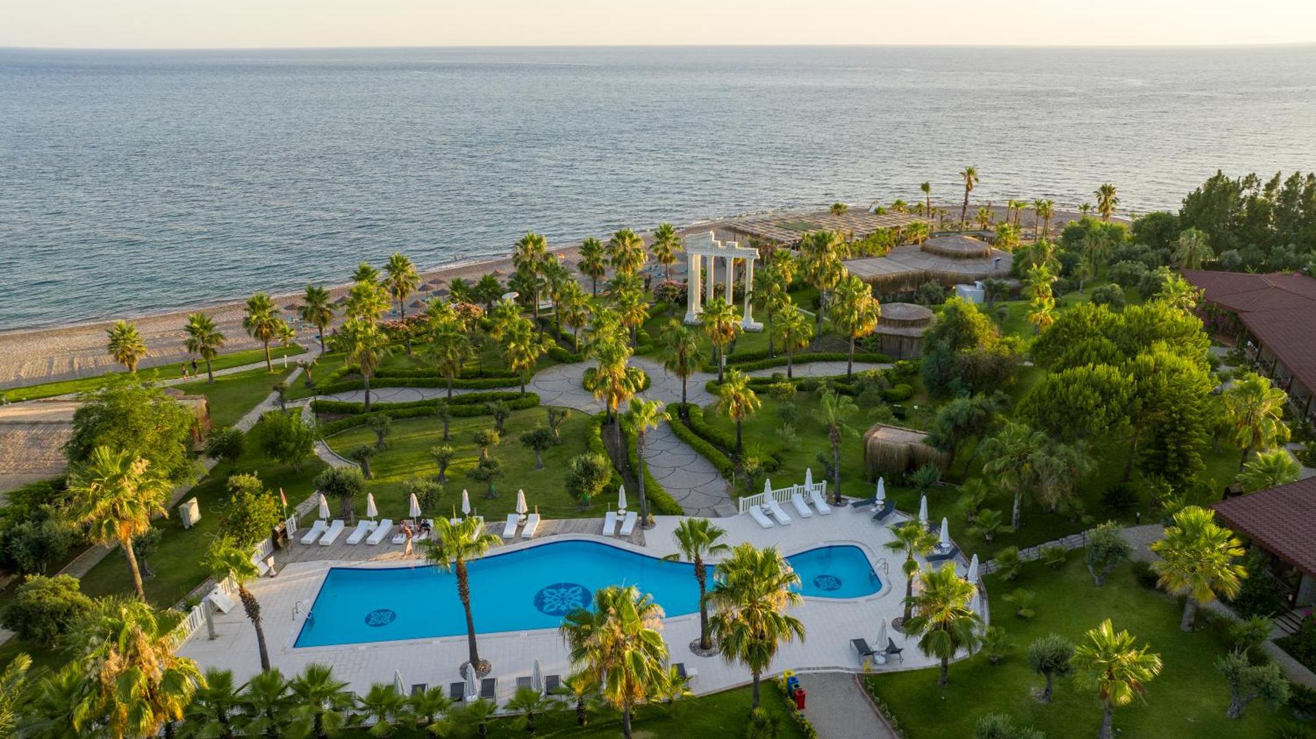 Flora Garden Beach panorāmas skats uz āra baseinu, palmu dārzu un Vidusjūras piekrasti saulrietā — plaša teritorija un atpūtas krēsli